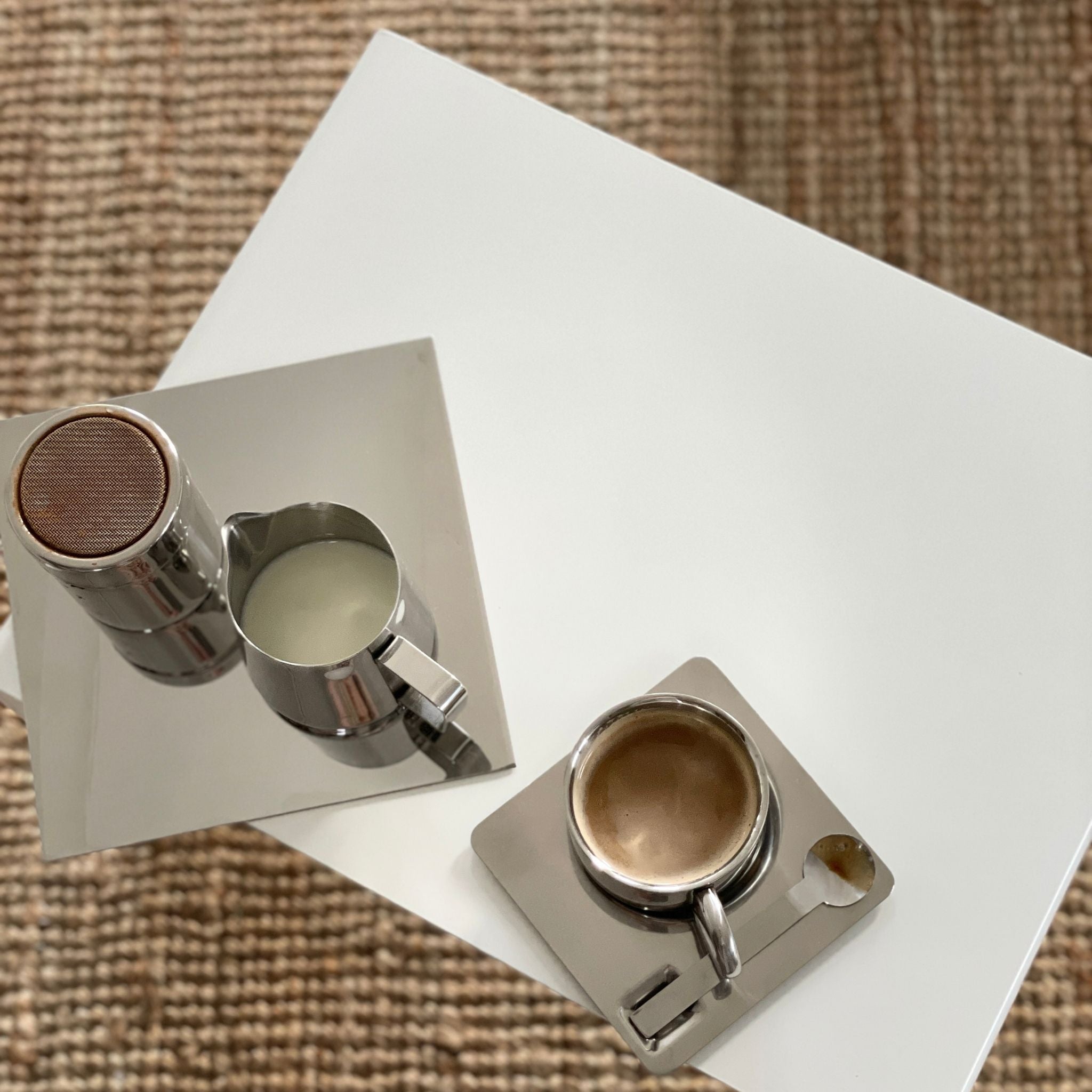 Detailaufnahme eines weißen Couchtisches mit Espressotasse, Milchkännchen und Spiegelplatte auf Naturteppich