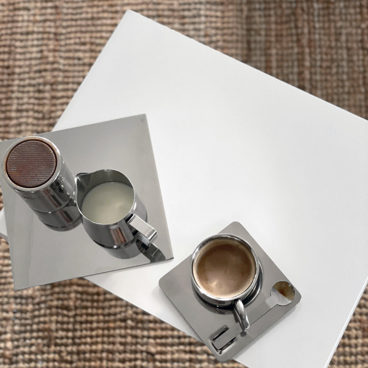 Detailaufnahme eines weißen Couchtisches mit Espressotasse, Milchkännchen und Spiegelplatte auf Naturteppich