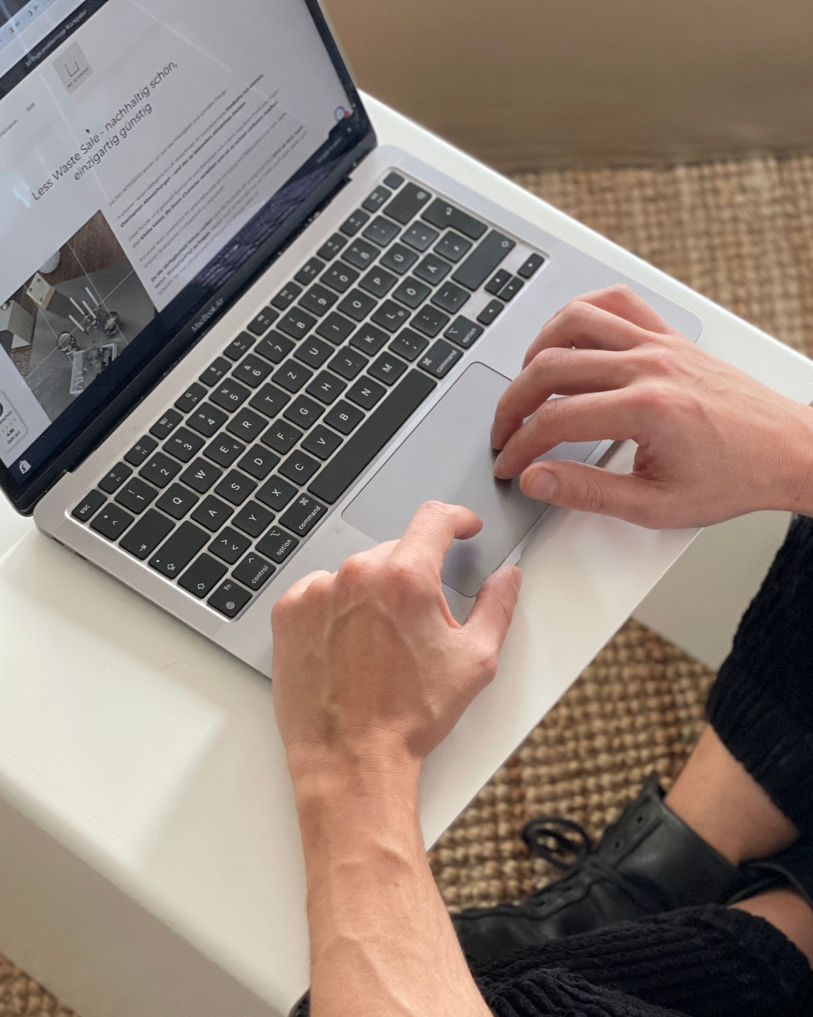 Arbeiten am Laptop auf einem weißen Couchtisch, minimalistische Einrichtung mit Naturteppich
