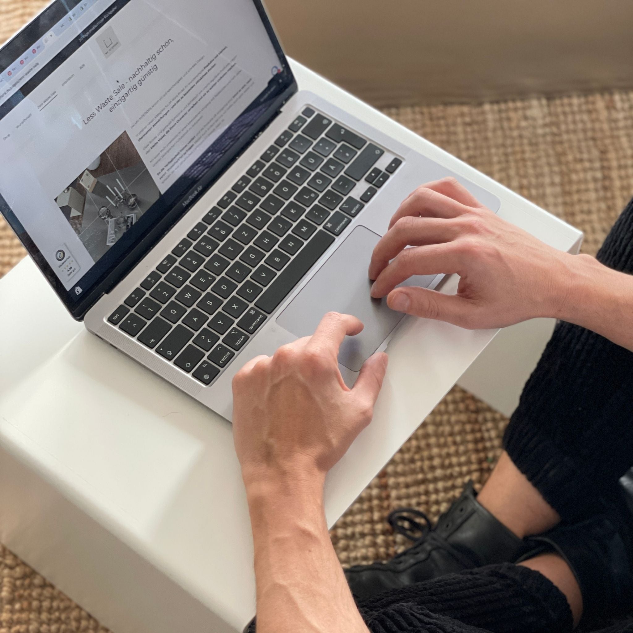 Arbeiten am Laptop auf einem weißen Couchtisch, minimalistische Einrichtung mit Naturteppich