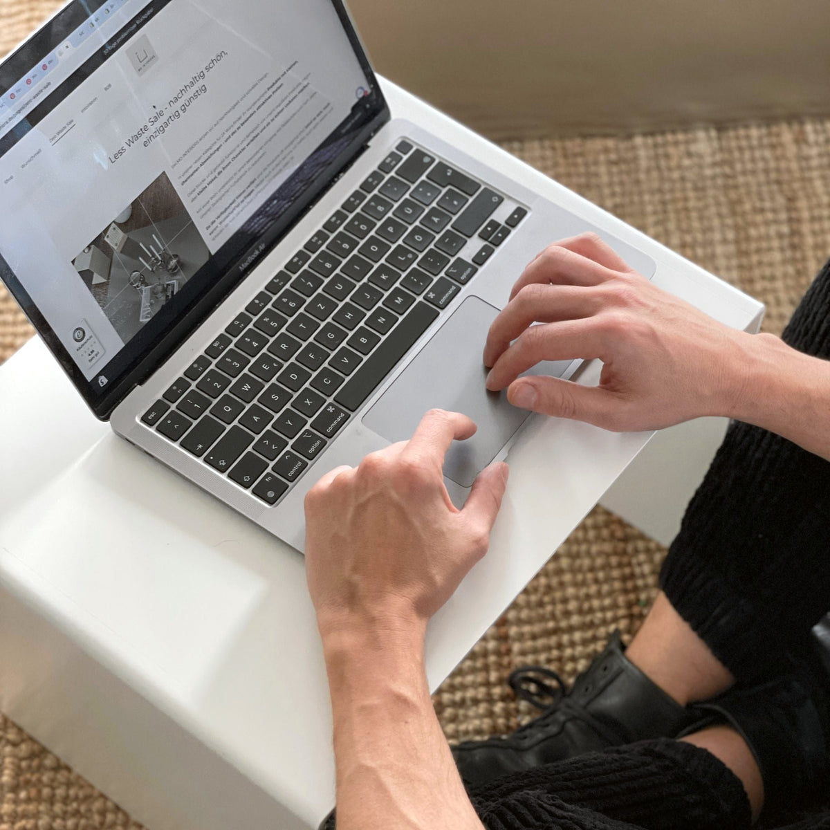 Arbeiten am Laptop auf einem weißen Couchtisch, minimalistische Einrichtung mit Naturteppich