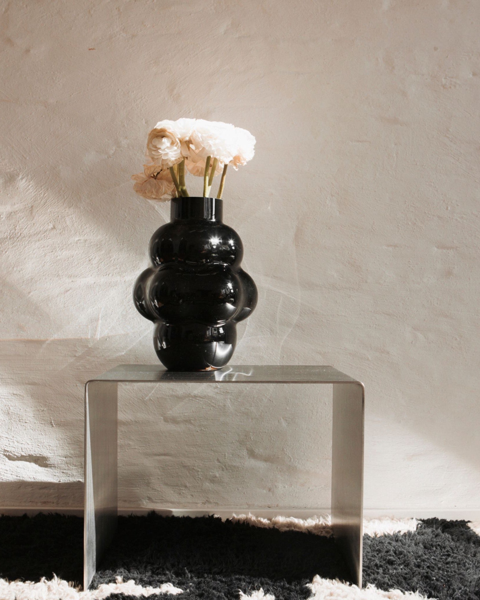 Edelstahl-Beistelltisch mit schwarzer Vase und weißen Blumen vor Naturwand