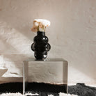 Edelstahl-Beistelltisch mit schwarzer Vase und weißen Blumen vor Naturwand