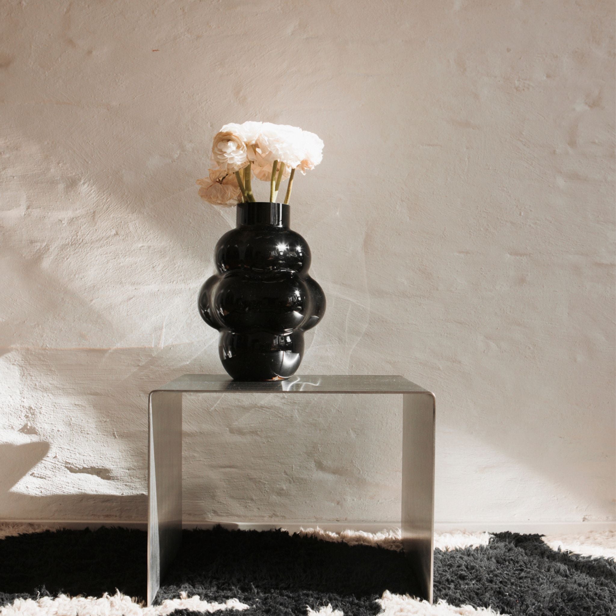 Edelstahl-Beistelltisch mit schwarzer Vase und weißen Blumen vor Naturwand