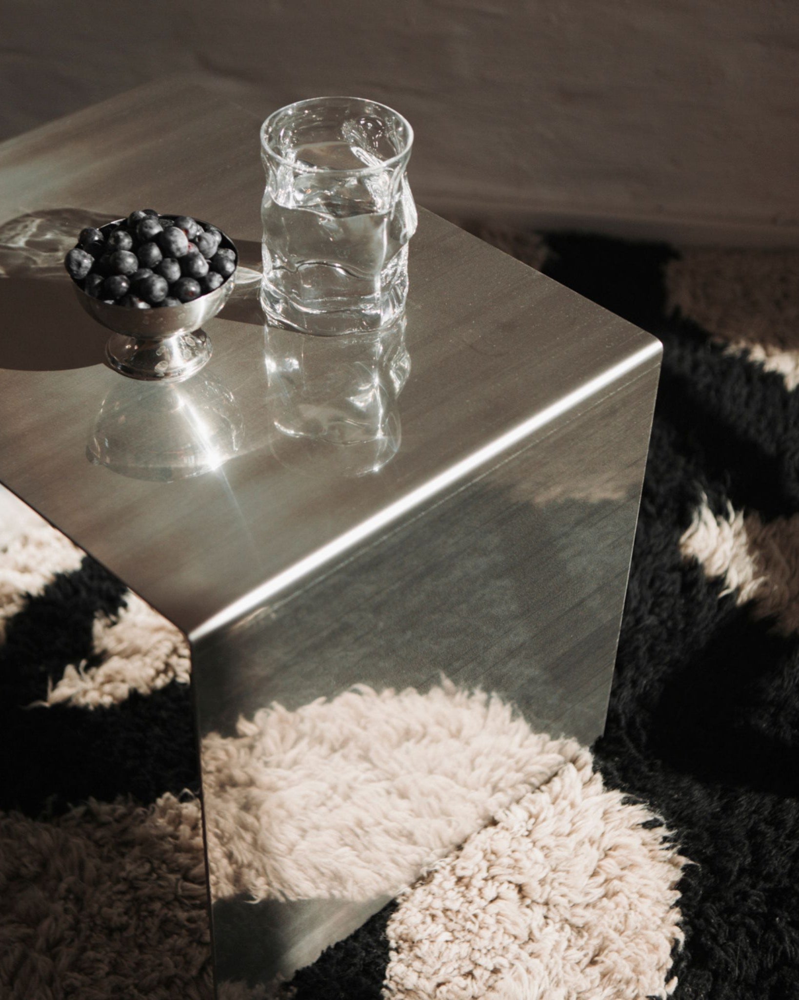 Minimalistischer Edelstahl-Hocker mit Wasser und Blaubeeren auf Teppich im Sonnenlicht