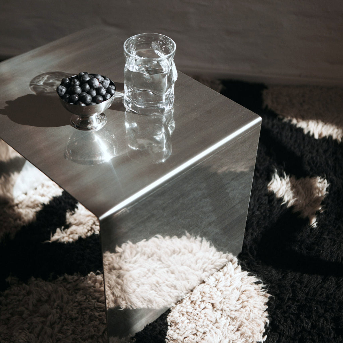 Minimalistischer Edelstahl-Hocker mit Wasser und Blaubeeren auf Teppich im Sonnenlicht
