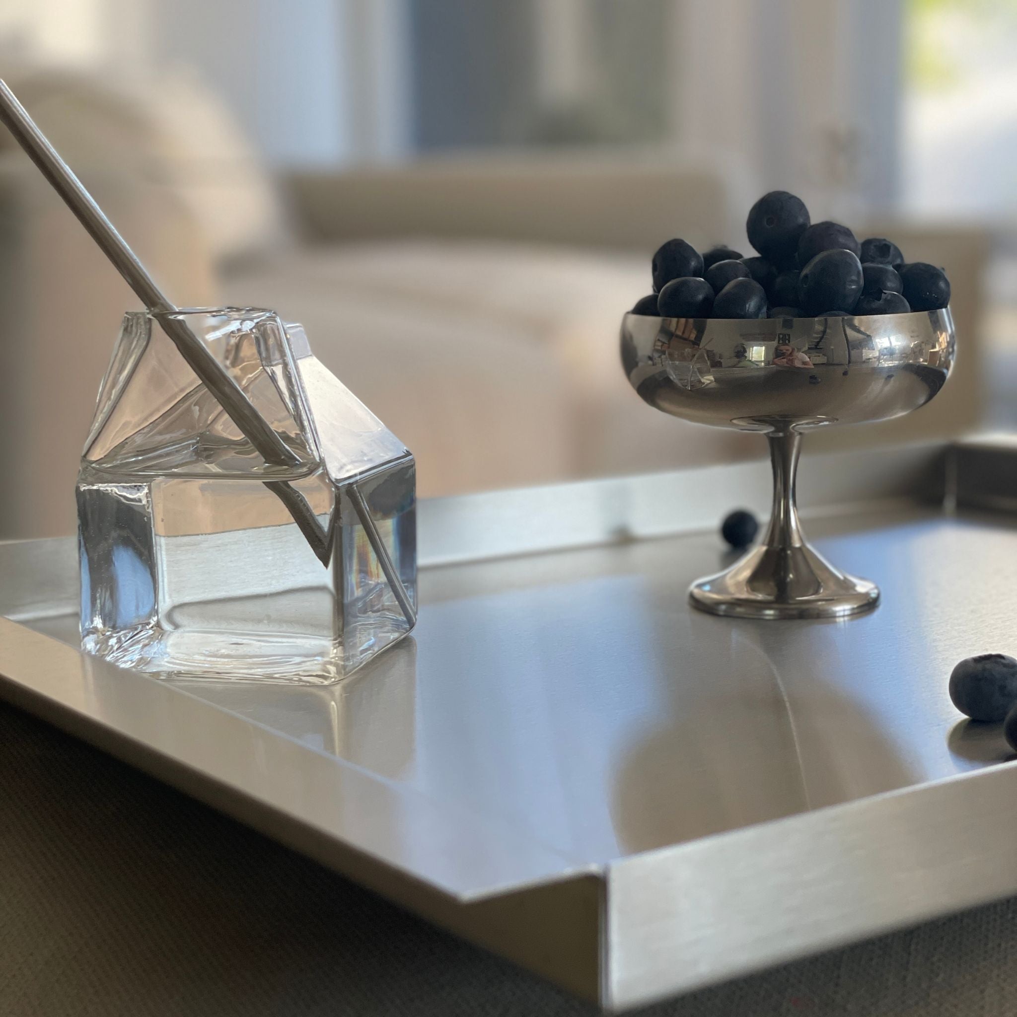 edelstahl tablett mit glassstrohhalm und blaubeeren auf stoffsofa