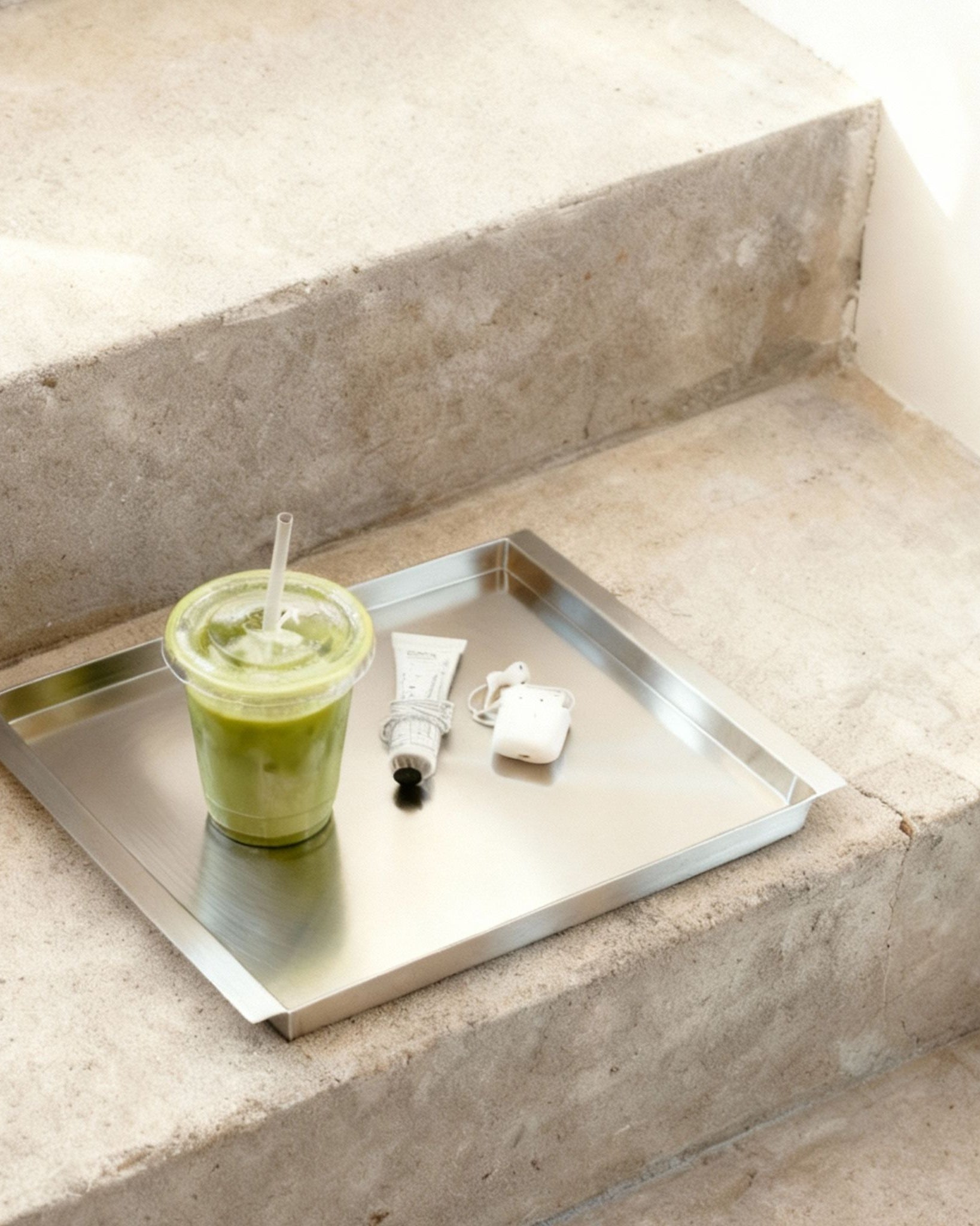 Edelstahl Tablett RAY mit Matcha Drink und Alltagsobjekten auf Betontreppe im minimalistischen Interior von MO INTERIORS