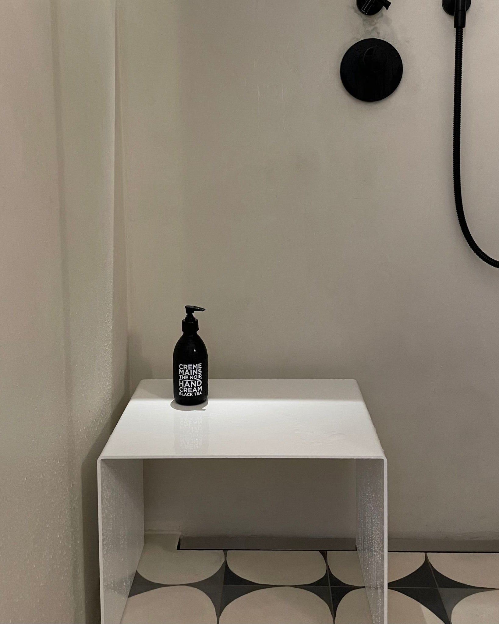 Weißer Hocker als Ablage in moderner Dusche mit schwarzer Armatur und Designfliesen