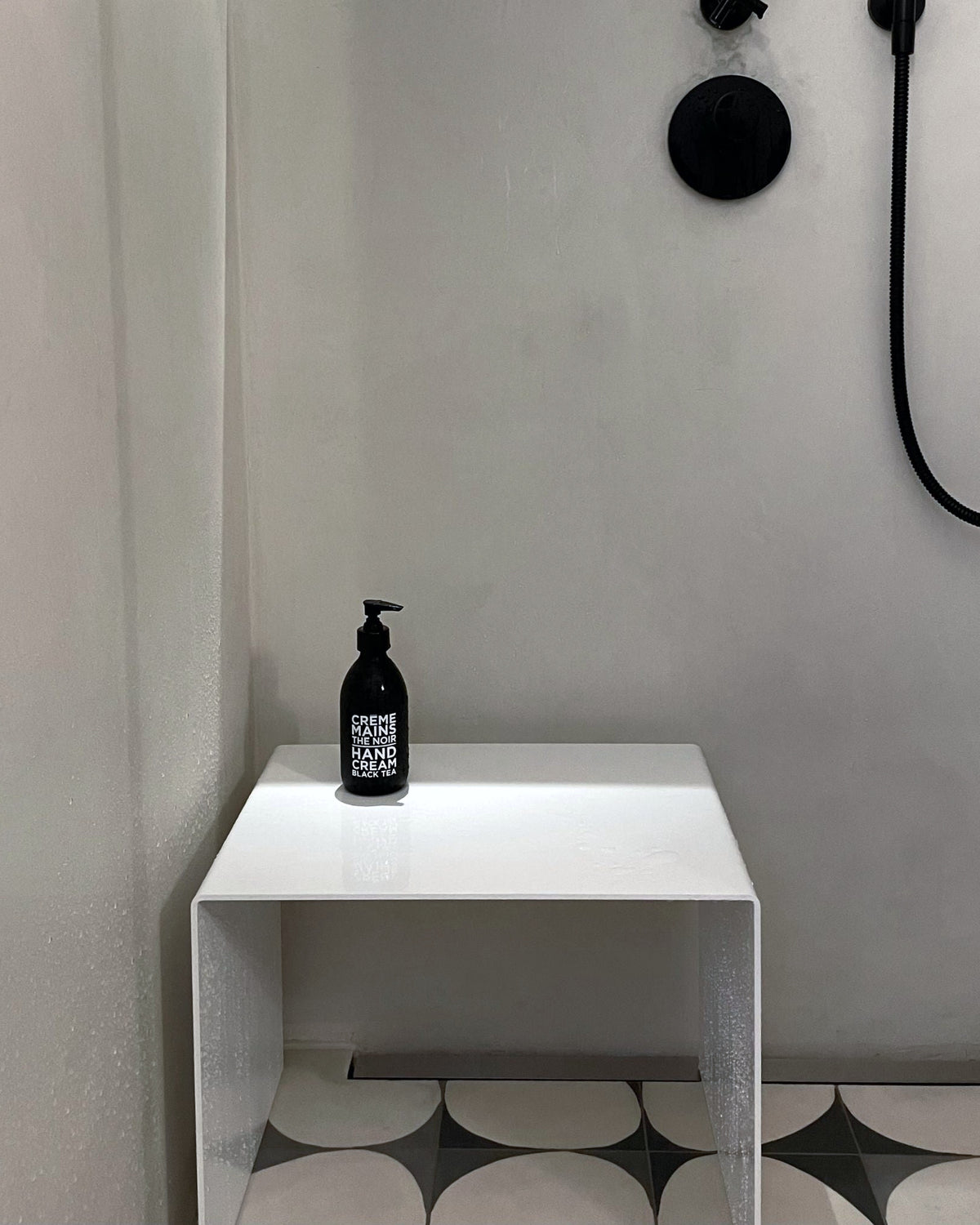 Weißer Hocker als Ablage in moderner Dusche mit schwarzer Armatur und Designfliesen