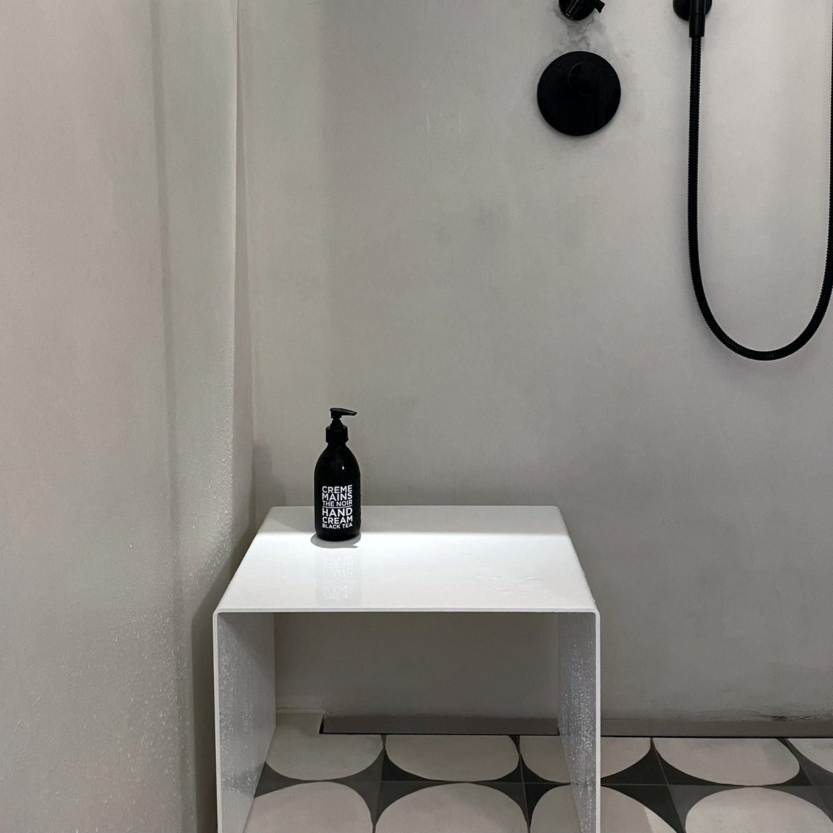 Weißer Hocker als Ablage in moderner Dusche mit schwarzer Armatur und Designfliesen