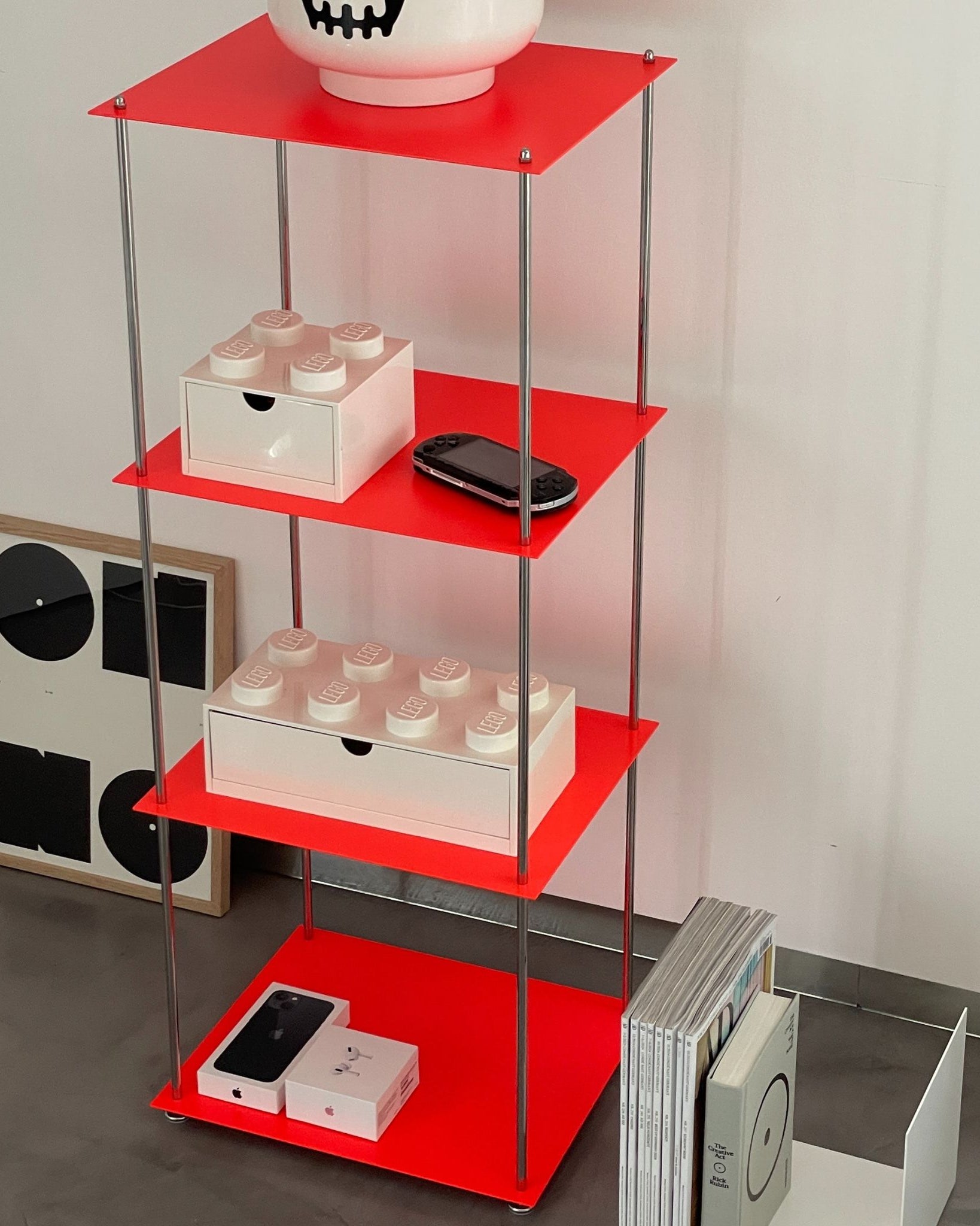 Rotes Regal mit Lego-Box, Konsole und Designmagazinen