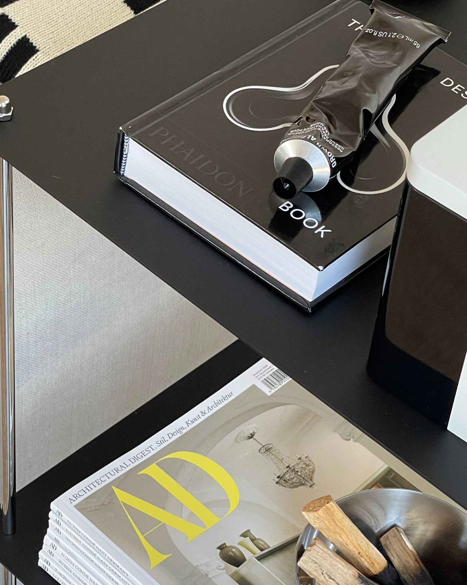 Detailansicht eines schwarzen pulverbeschichteten Regals mit Designbuch und Deko im Wohnzimmer