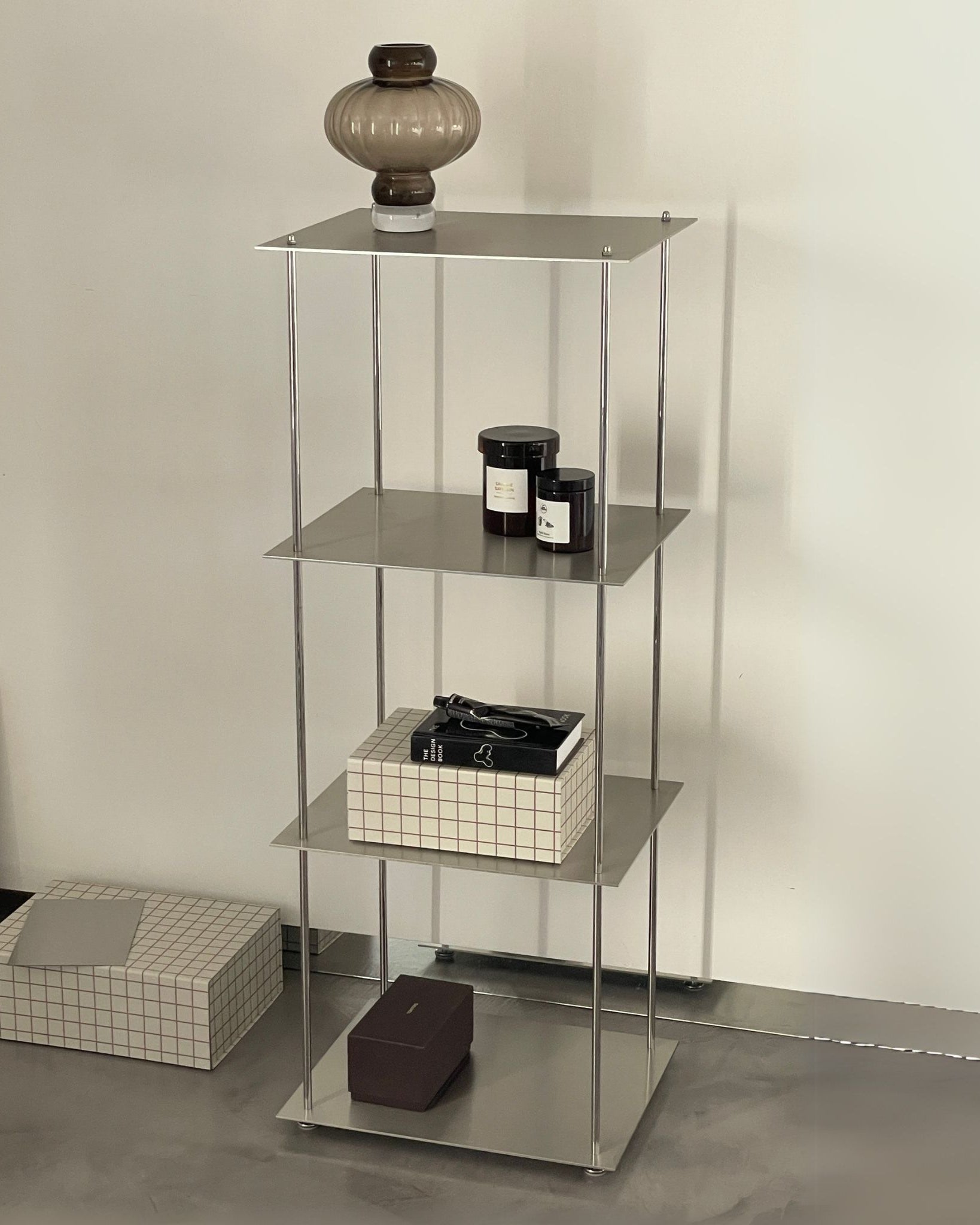 Modernes Edelstahl-Regalsystem mit Deko-Objekten und Glaslampe in minimalistischem Interior