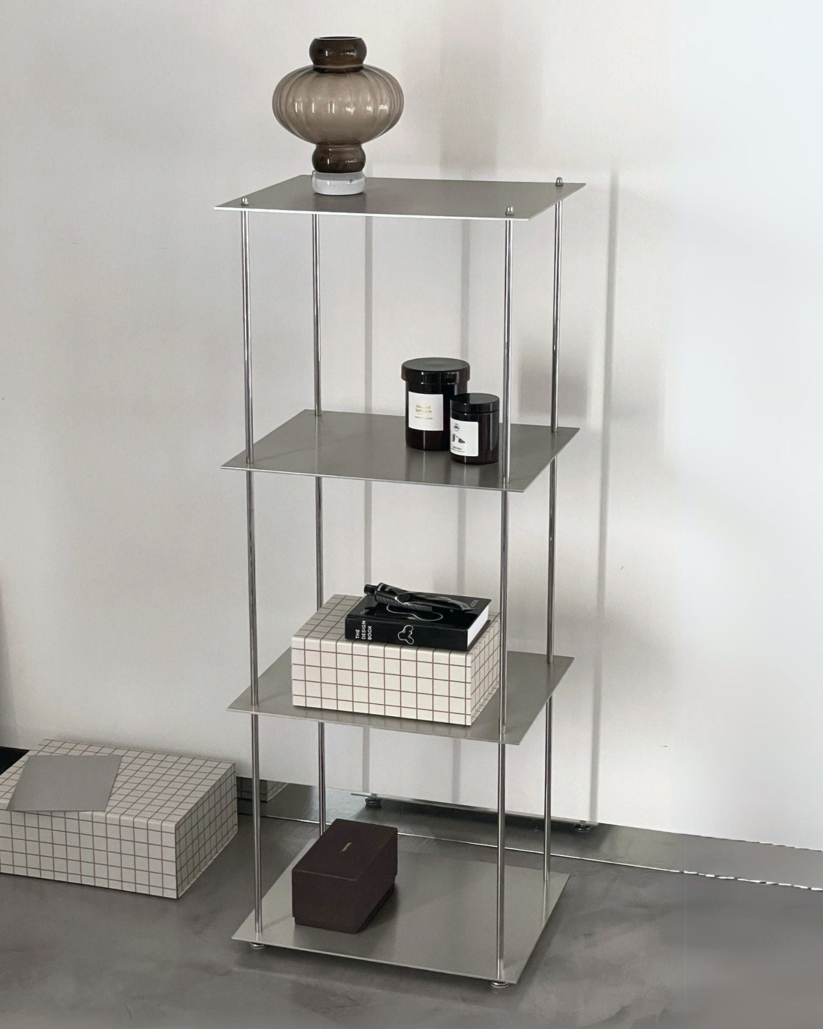 Modernes Edelstahl-Regalsystem mit Deko-Objekten und Glaslampe in minimalistischem Interior