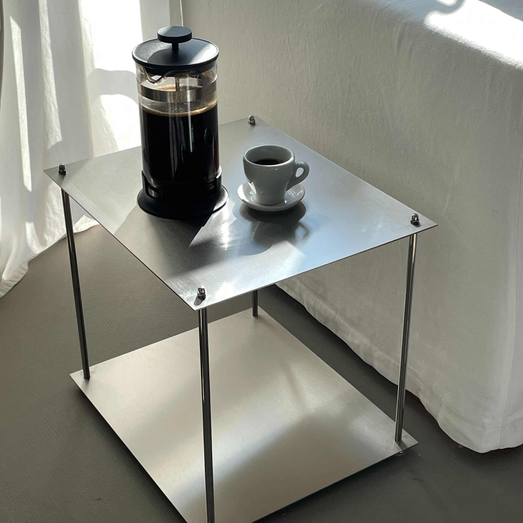 Französische Presse und Kaffeetasse auf einem minimalistischen, quadratischen Modulum Beistelltisch aus Edelstahl mit Ablage.