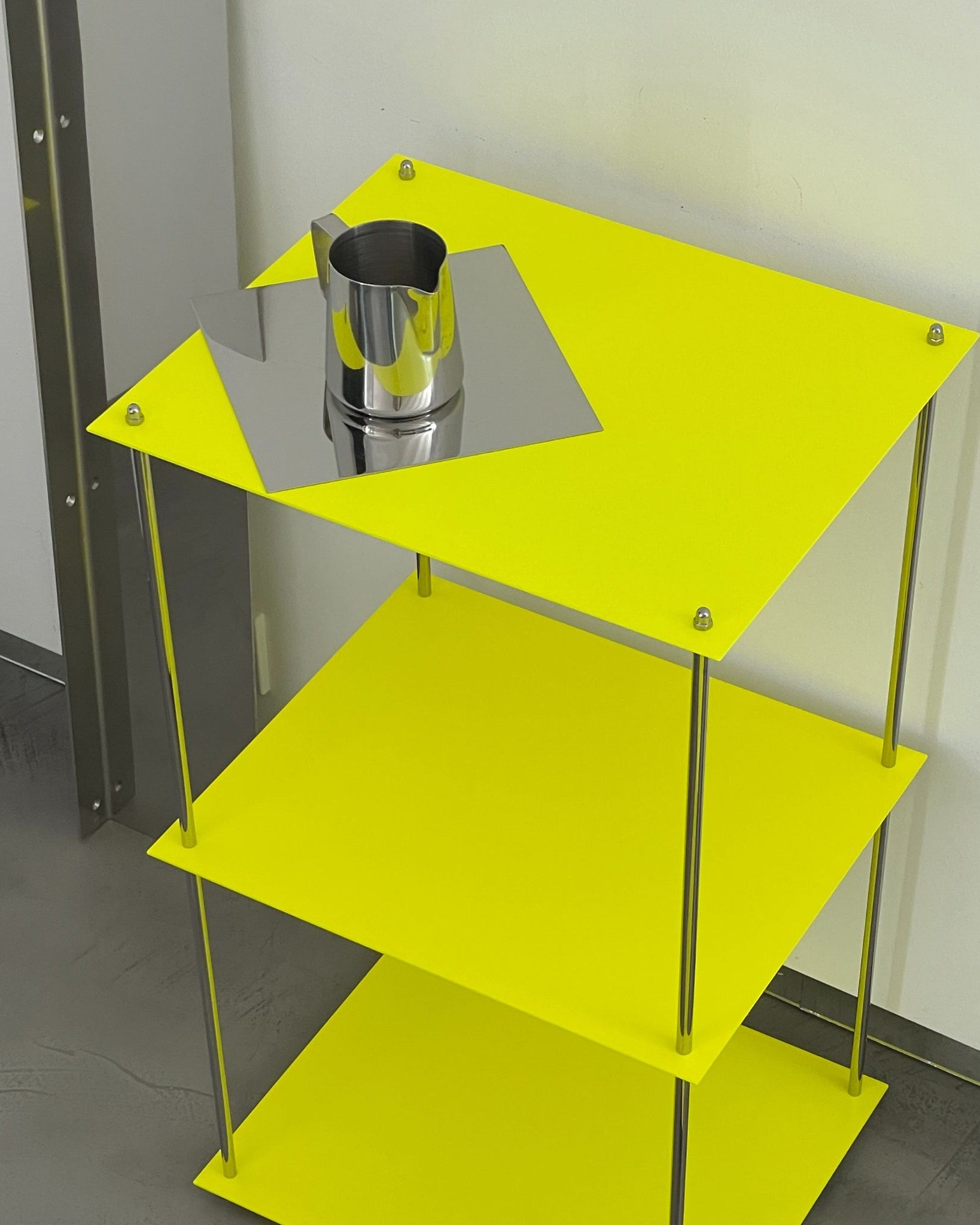 Detailansicht MODULUM Regal in Leuchtgelb mit Edelstahlkanne auf spiegelnder Ablagefläche