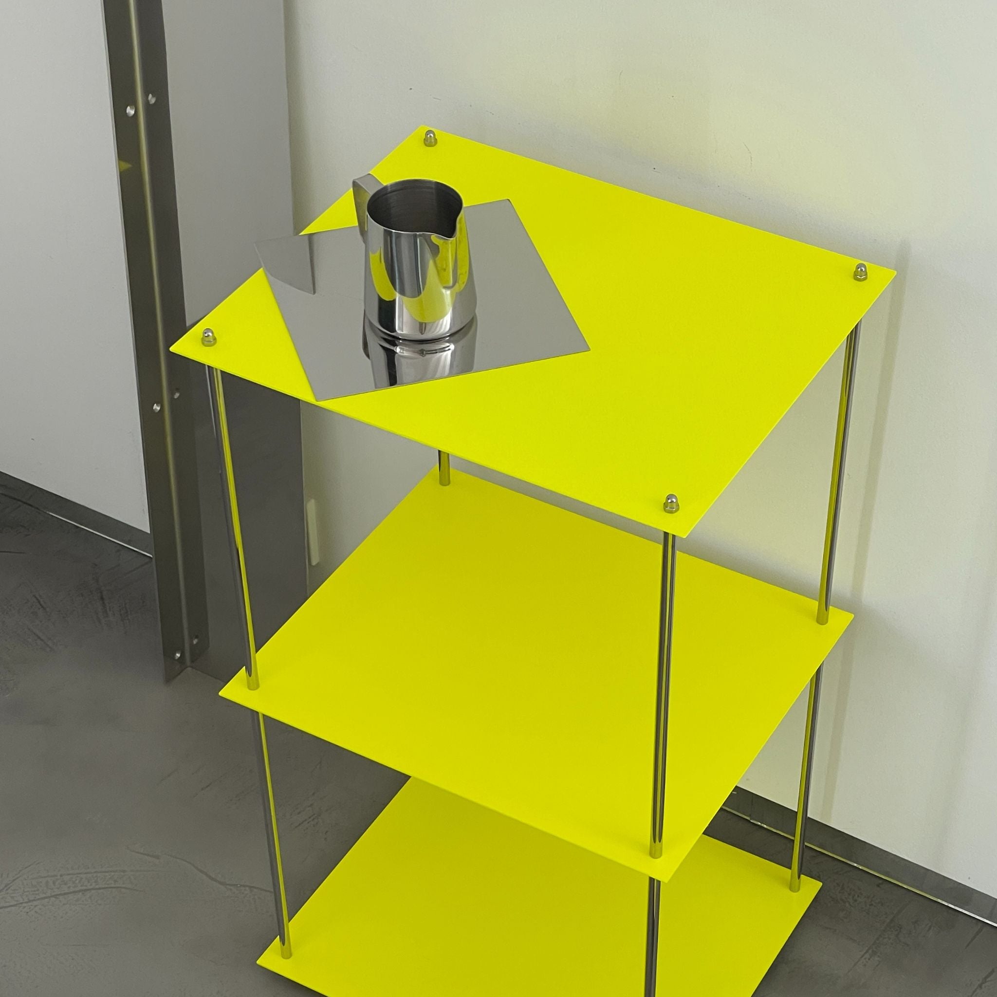 Detailansicht MODULUM Regal in Leuchtgelb mit Edelstahlkanne auf spiegelnder Ablagefläche