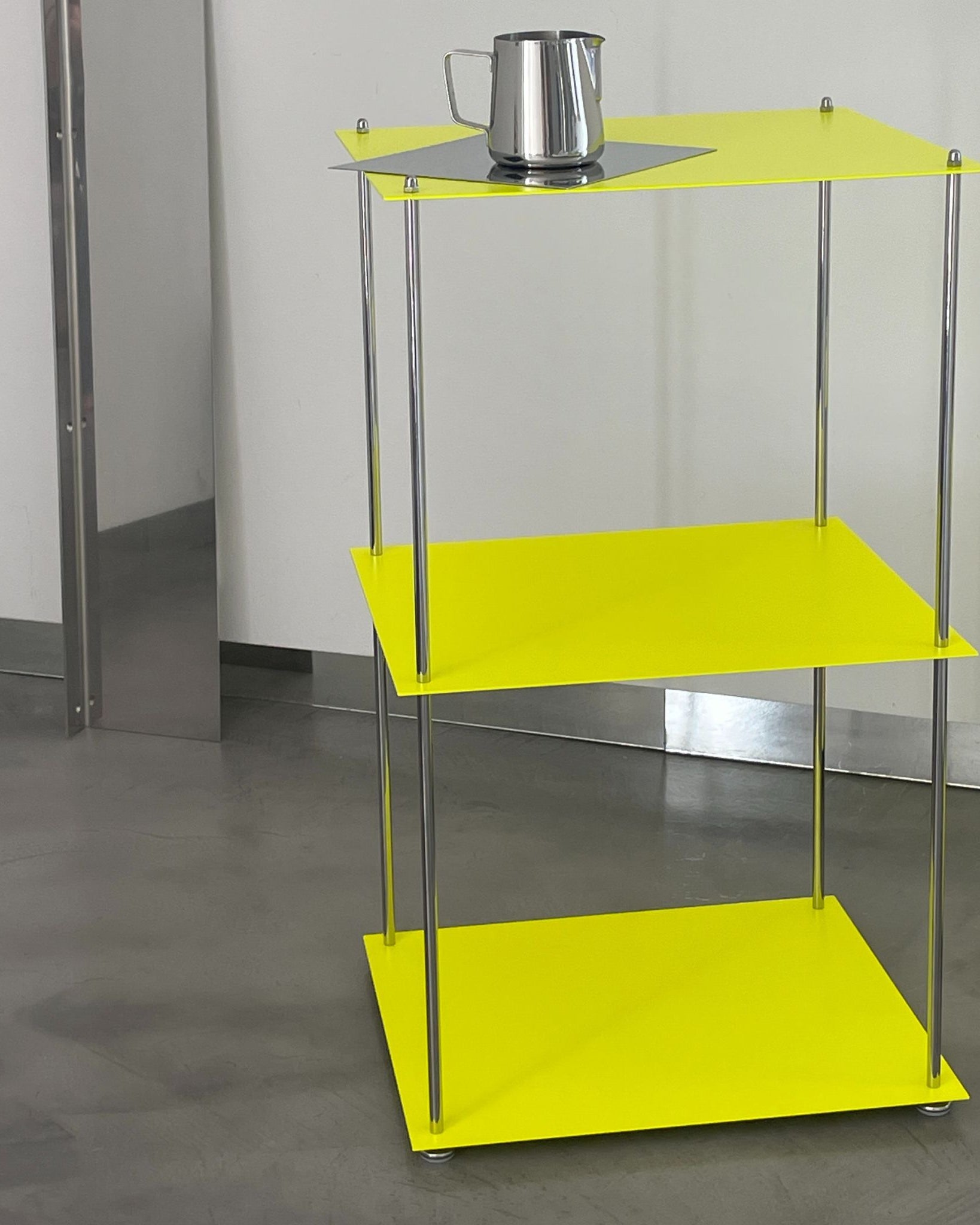 MODULUM Regal in Leuchtgelb mit Edelstahlkanne auf oberster Ebene vor heller Wand und Spiegelobjekt