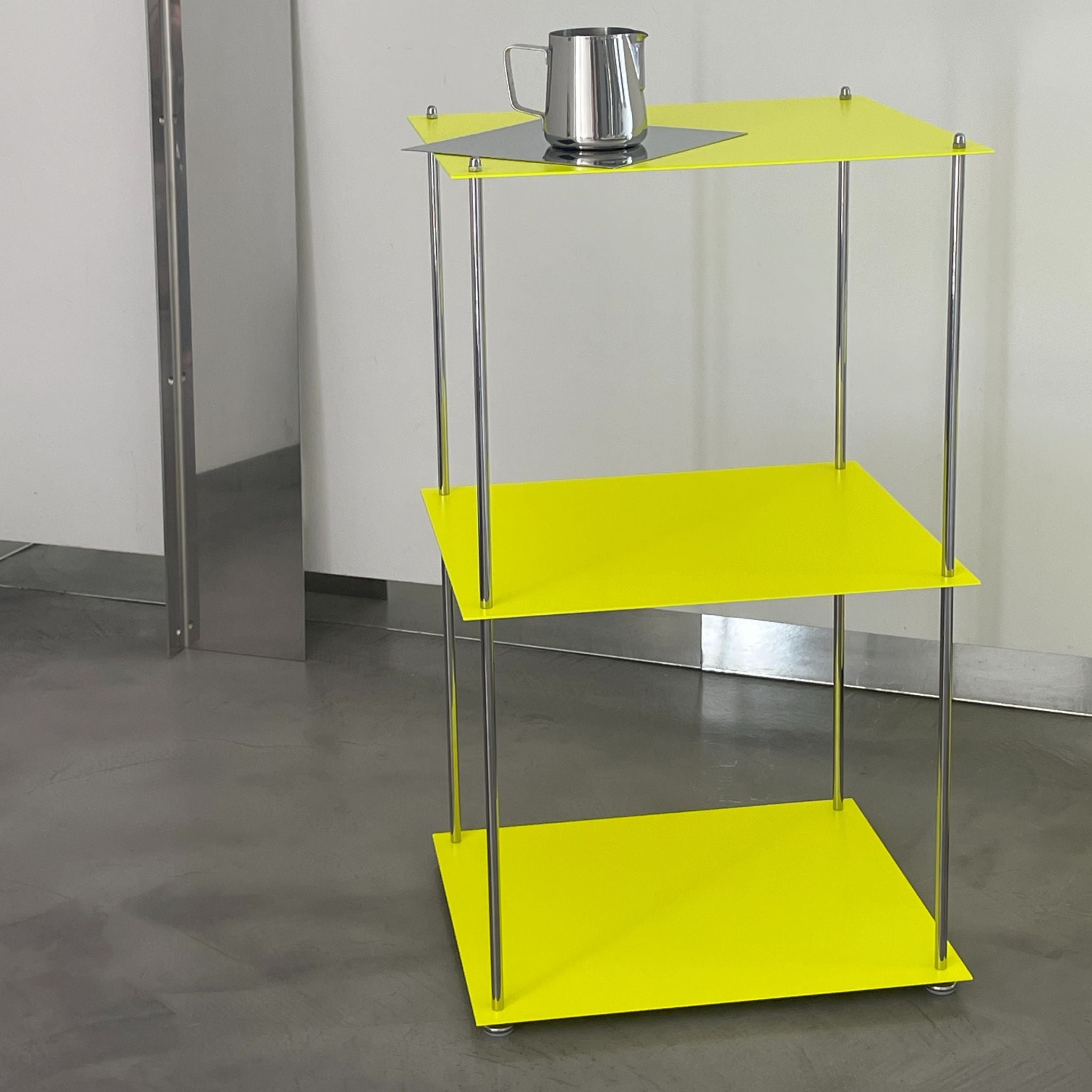 MODULUM Regal in Leuchtgelb mit Edelstahlkanne auf oberster Ebene vor heller Wand und Spiegelobjekt