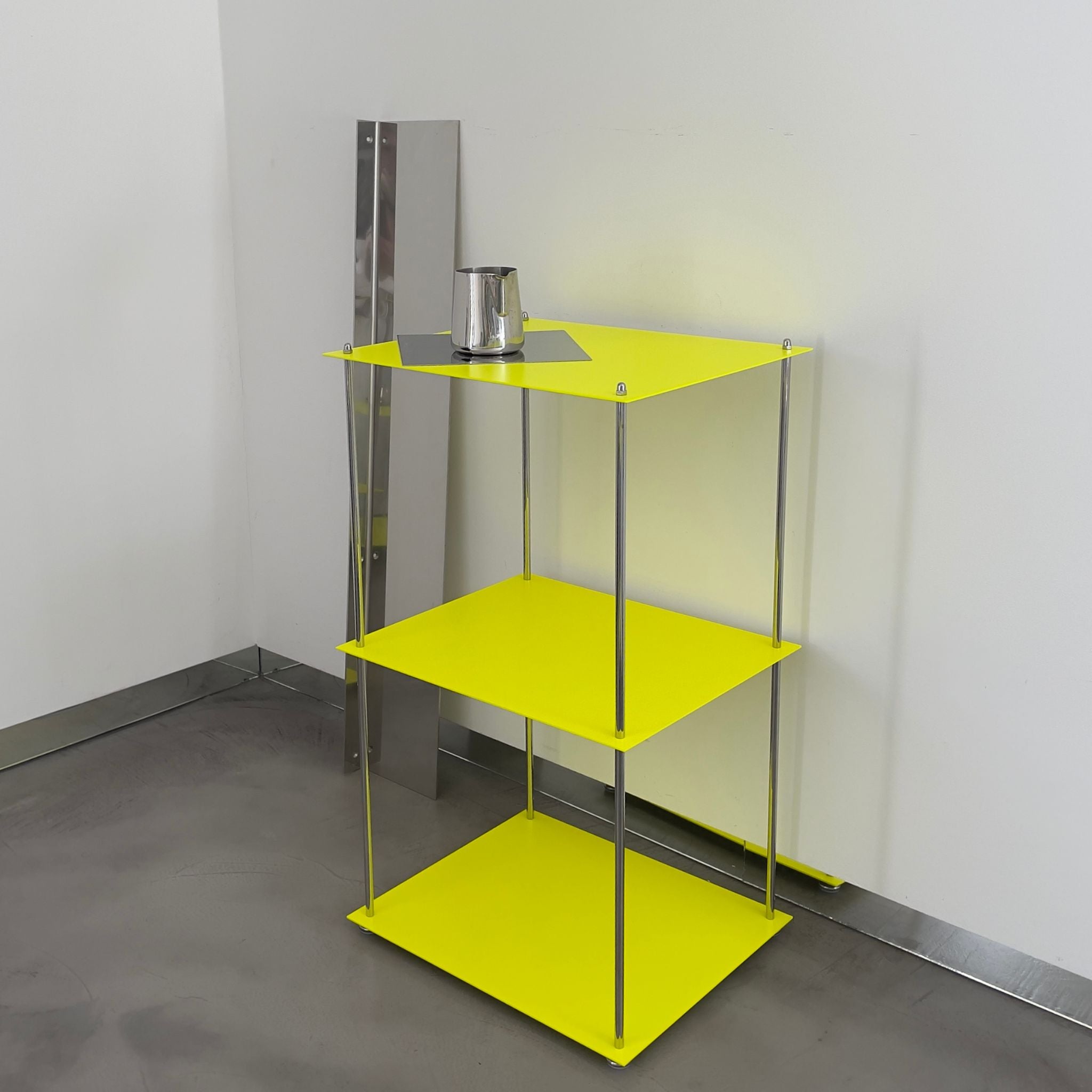 Leuchtgelbes MODULUM Regal mit Edelstahlkanne, seitlich gespiegelt, vor heller Wand in minimalistischem Setting