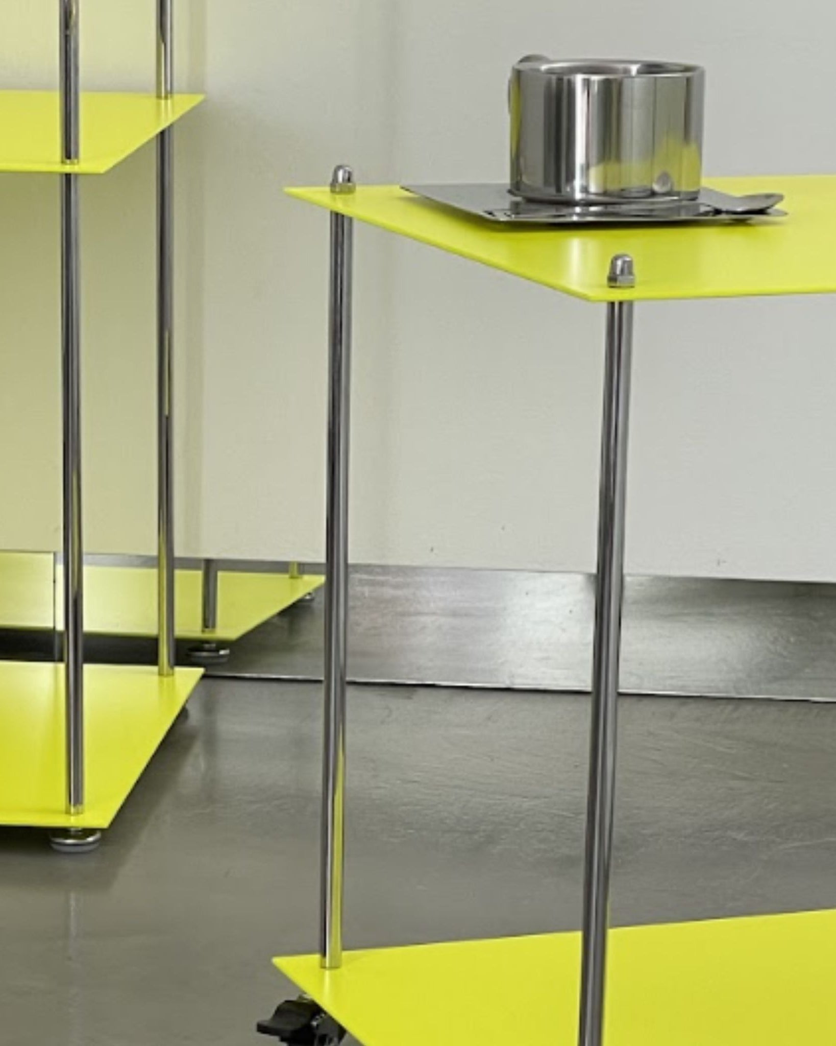 Detailansicht des leuchtgelben Modulum Regals mit Edelstahlstreben und Rollen auf grauem Boden