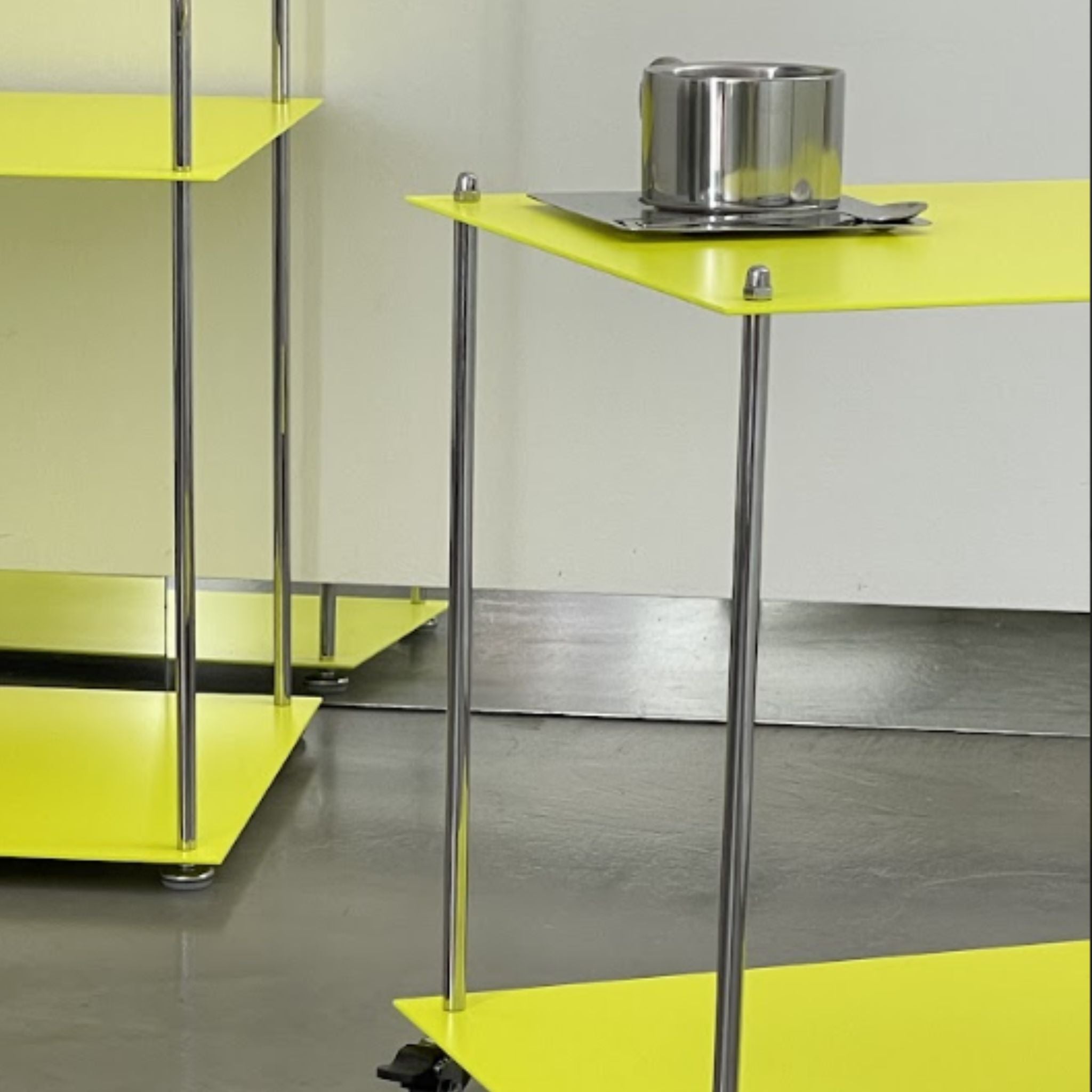 Detailansicht des leuchtgelben Modulum Regals mit Edelstahlstreben und Rollen auf grauem Boden