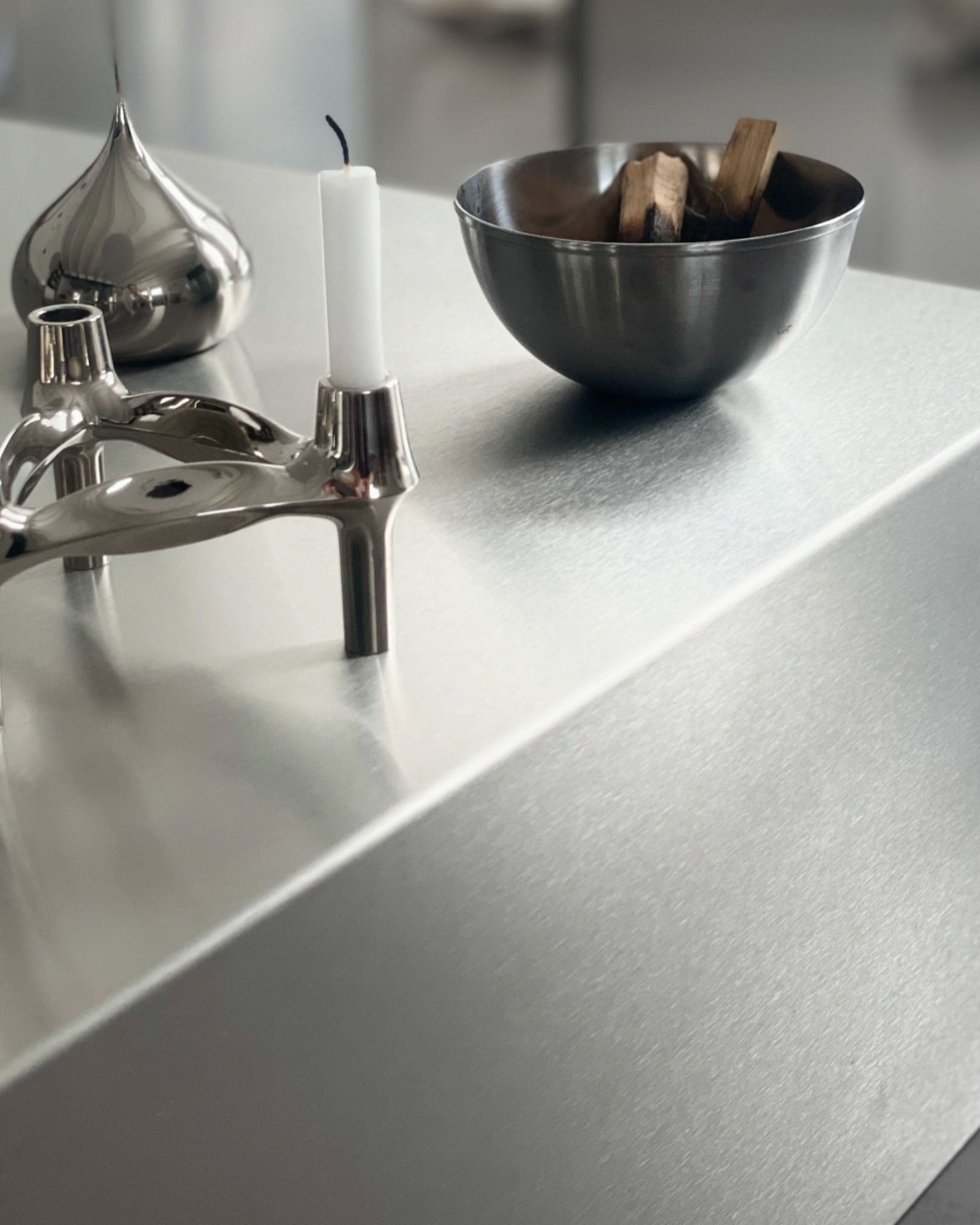 Detailaufnahme einer gebürsteten Edelstahloberfläche mit Kerzenhalter und Schale