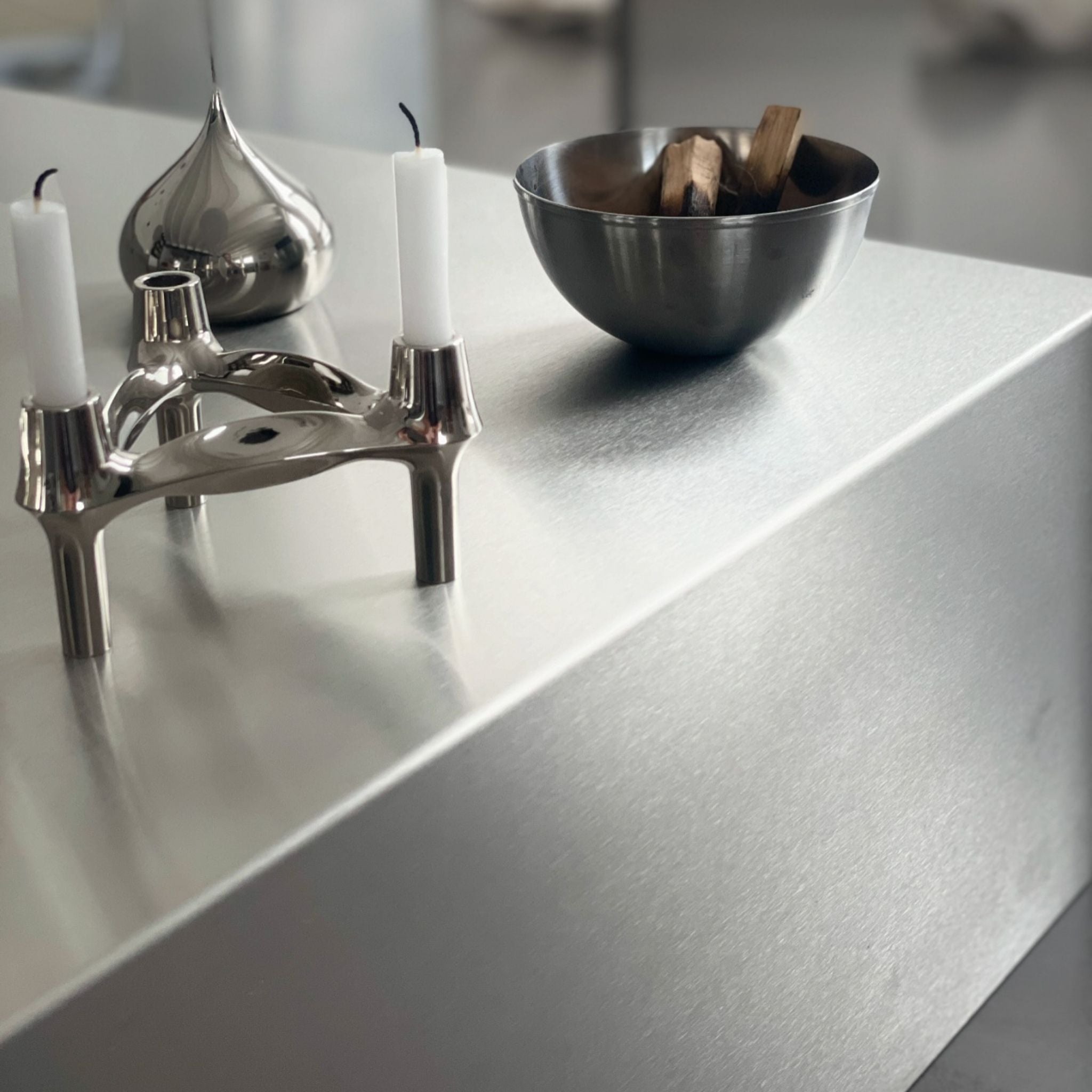 Detailaufnahme einer gebürsteten Edelstahloberfläche mit Kerzenhalter und Schale