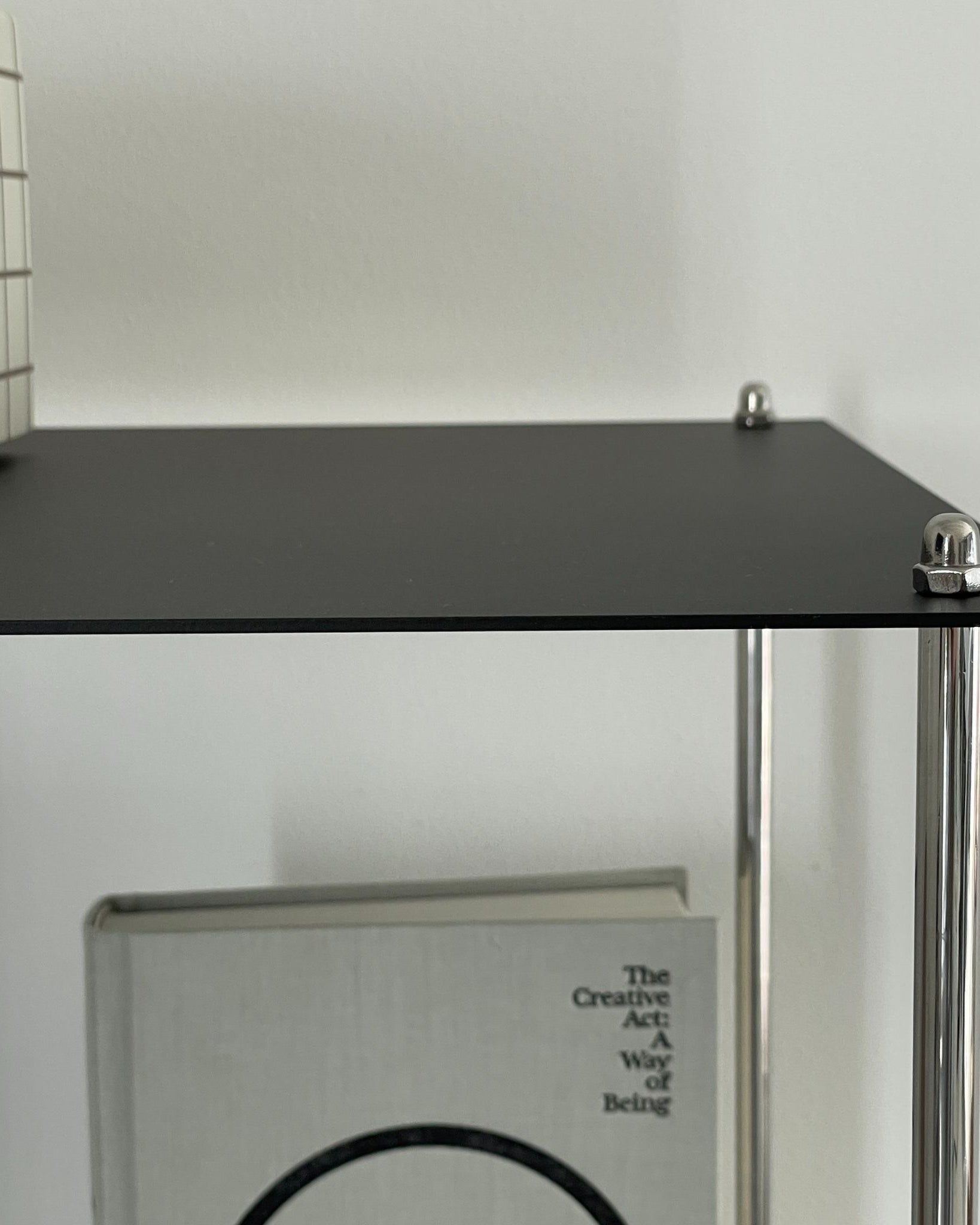 Detailansicht eines schwarzen Stahlregals mit Edelstahlstreben und dekorativem Buch im minimalistischen Interieur