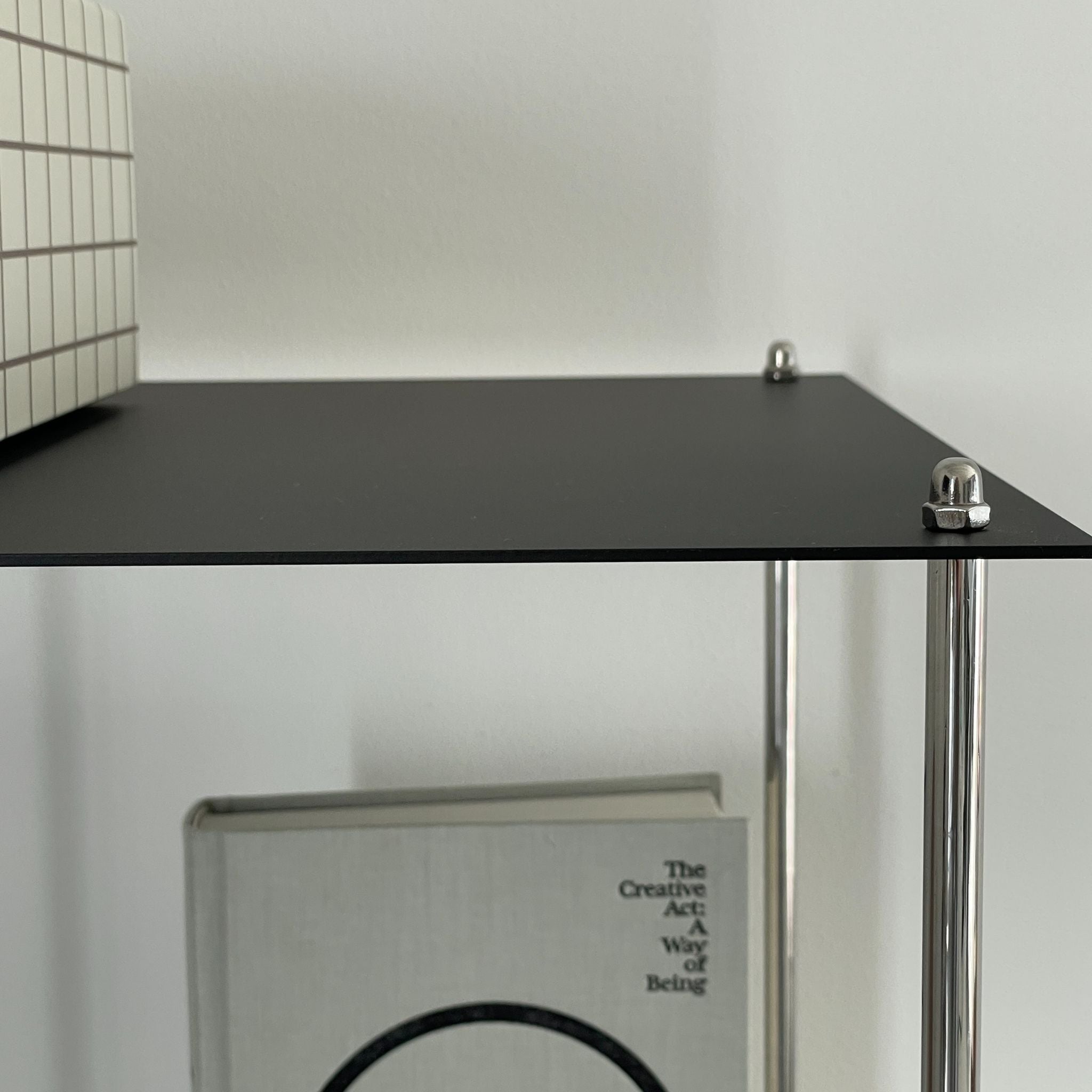 Detailansicht eines schwarzen Stahlregals mit Edelstahlstreben und dekorativem Buch im minimalistischen Interieur