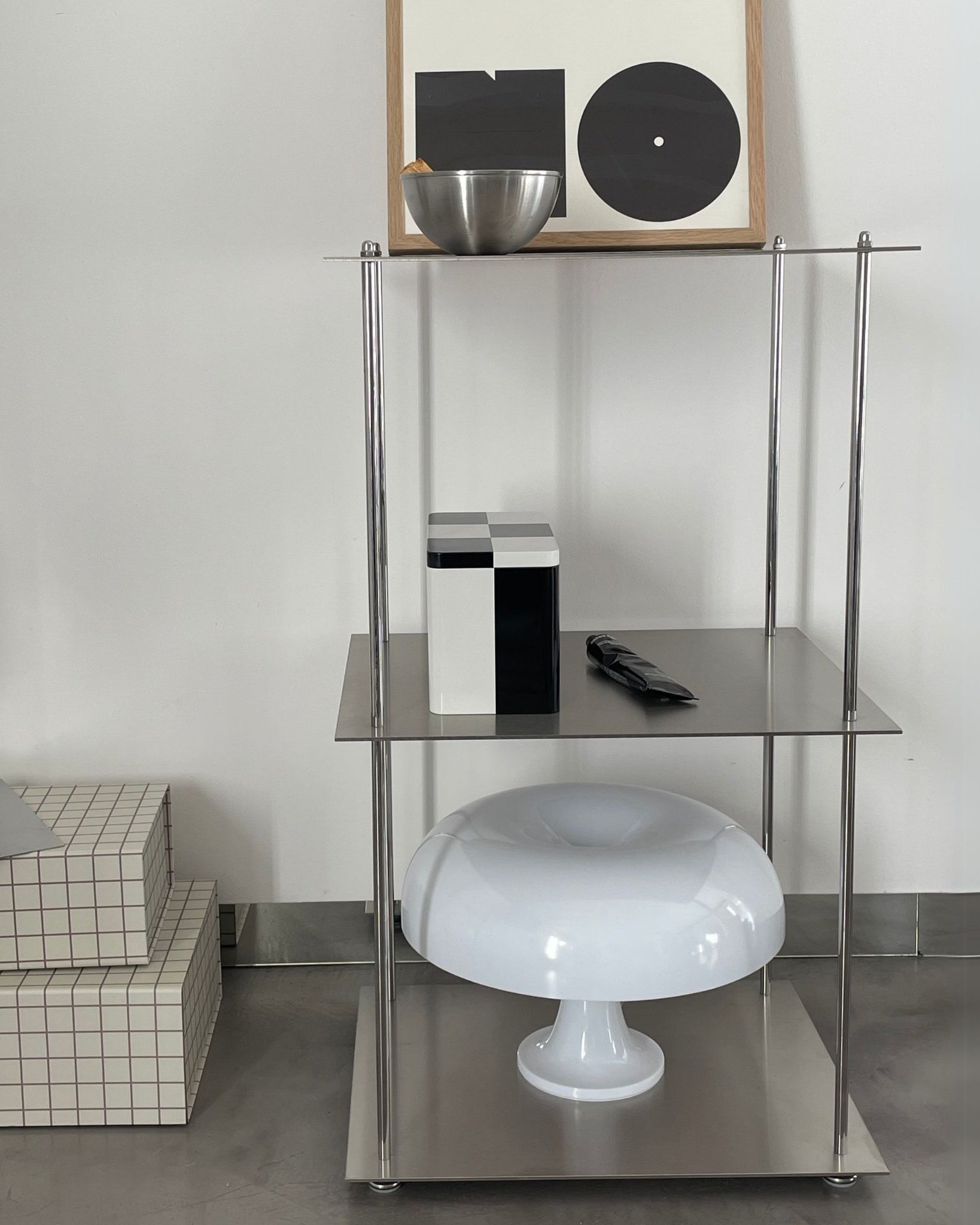 Modulares Edelstahl-Regalsystem mit Designobjekten und Pilzlampe vor einer weißen Wand
