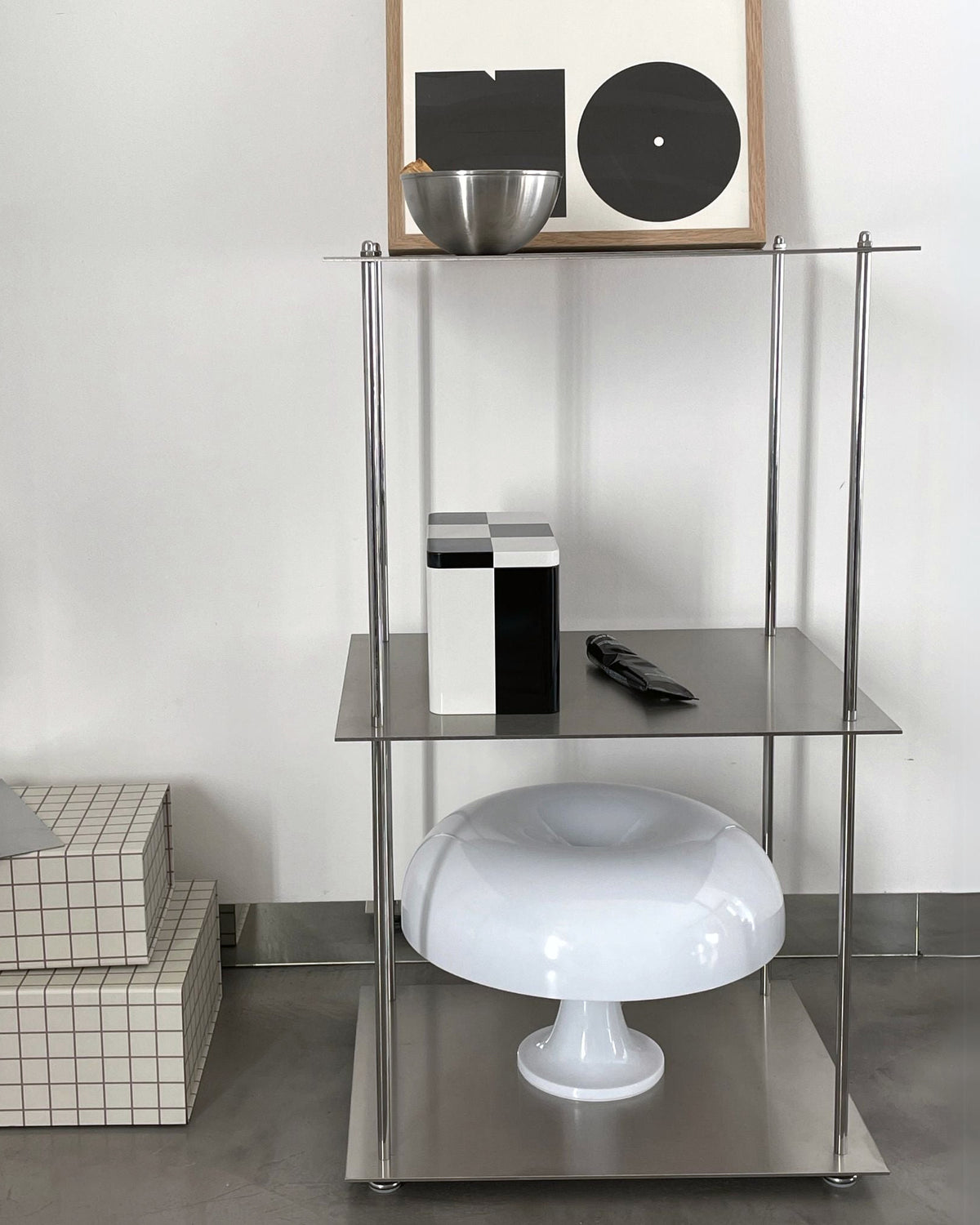 Modulares Edelstahl-Regalsystem mit Designobjekten und Pilzlampe vor einer weißen Wand