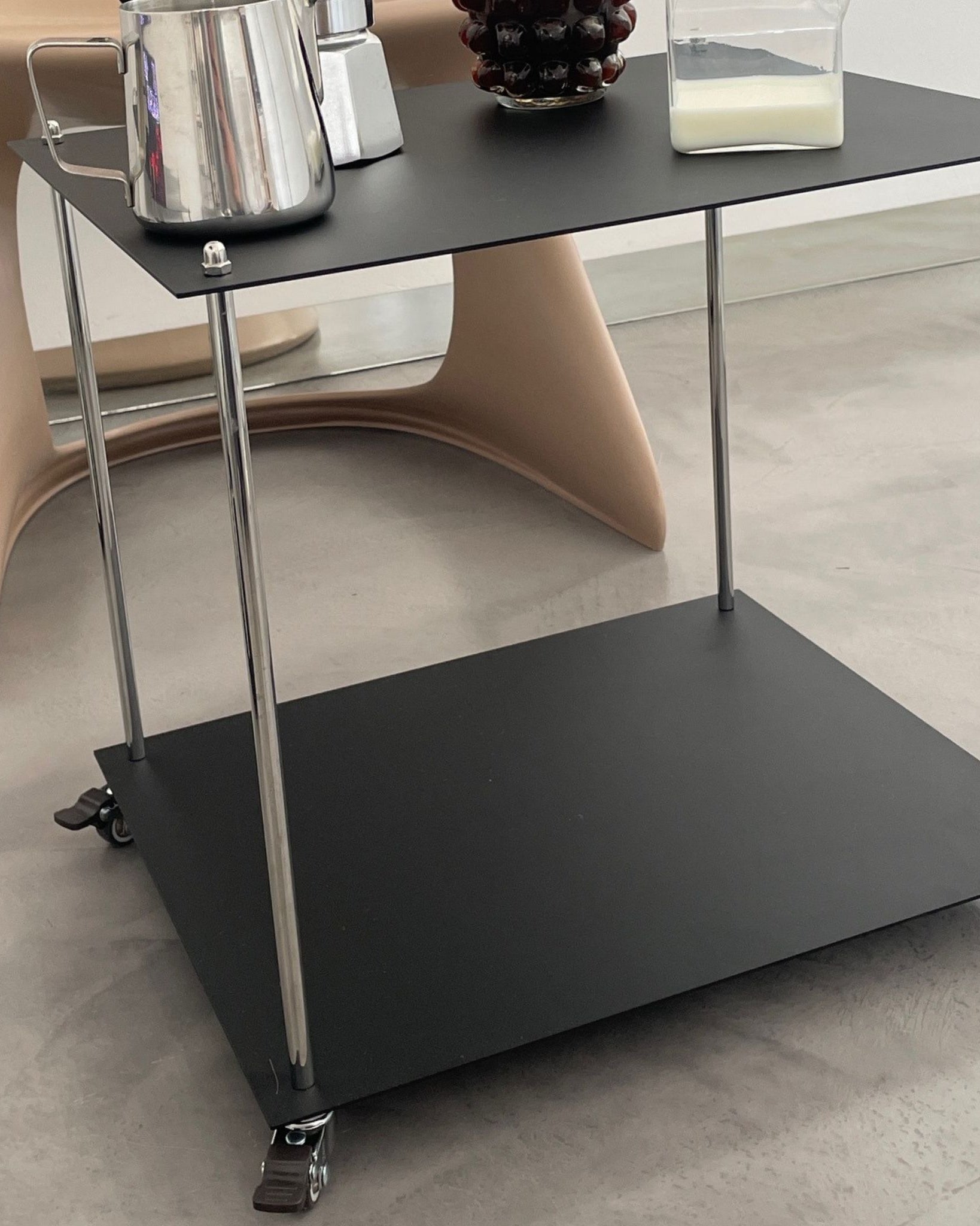 Moderner Servierwagen aus schwarzem Stahl mit Rollen im minimalistischen Interior neben Designstuhl und Kaffeegeschirr