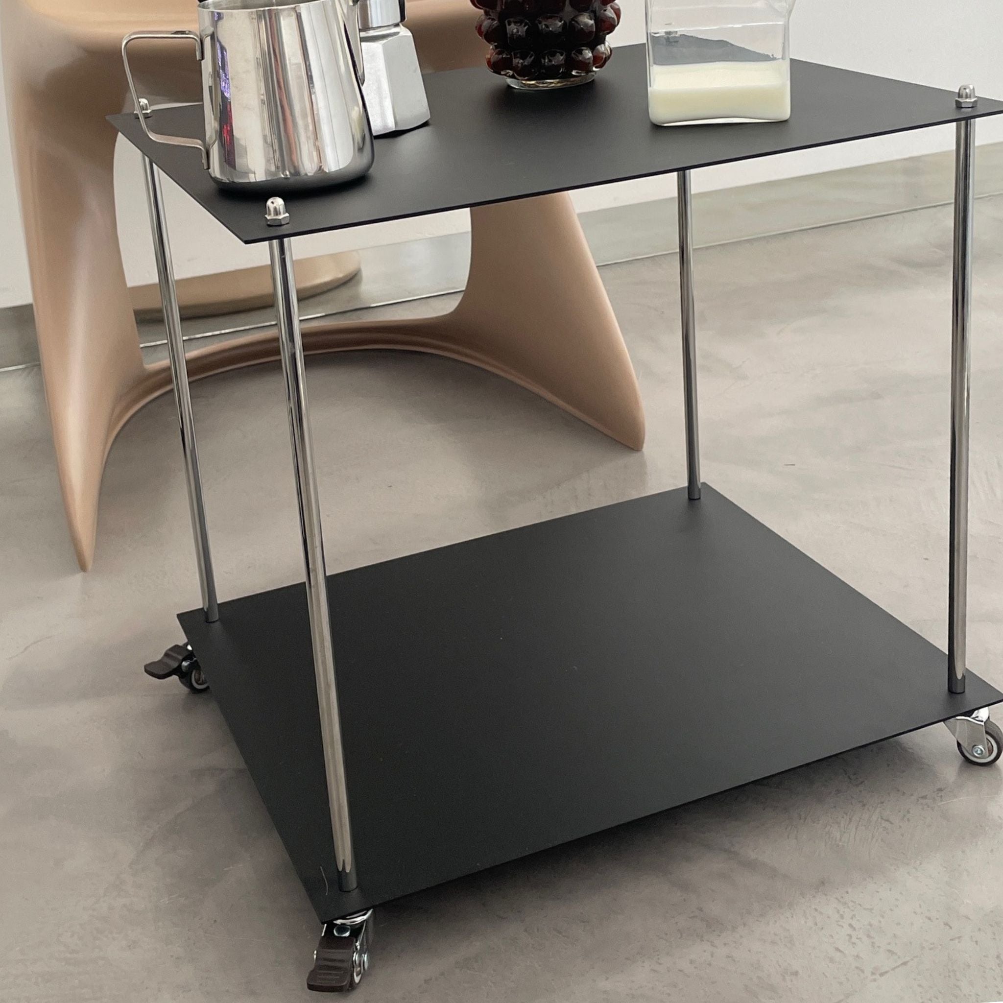 Moderner Servierwagen aus schwarzem Stahl mit Rollen im minimalistischen Interior neben Designstuhl und Kaffeegeschirr