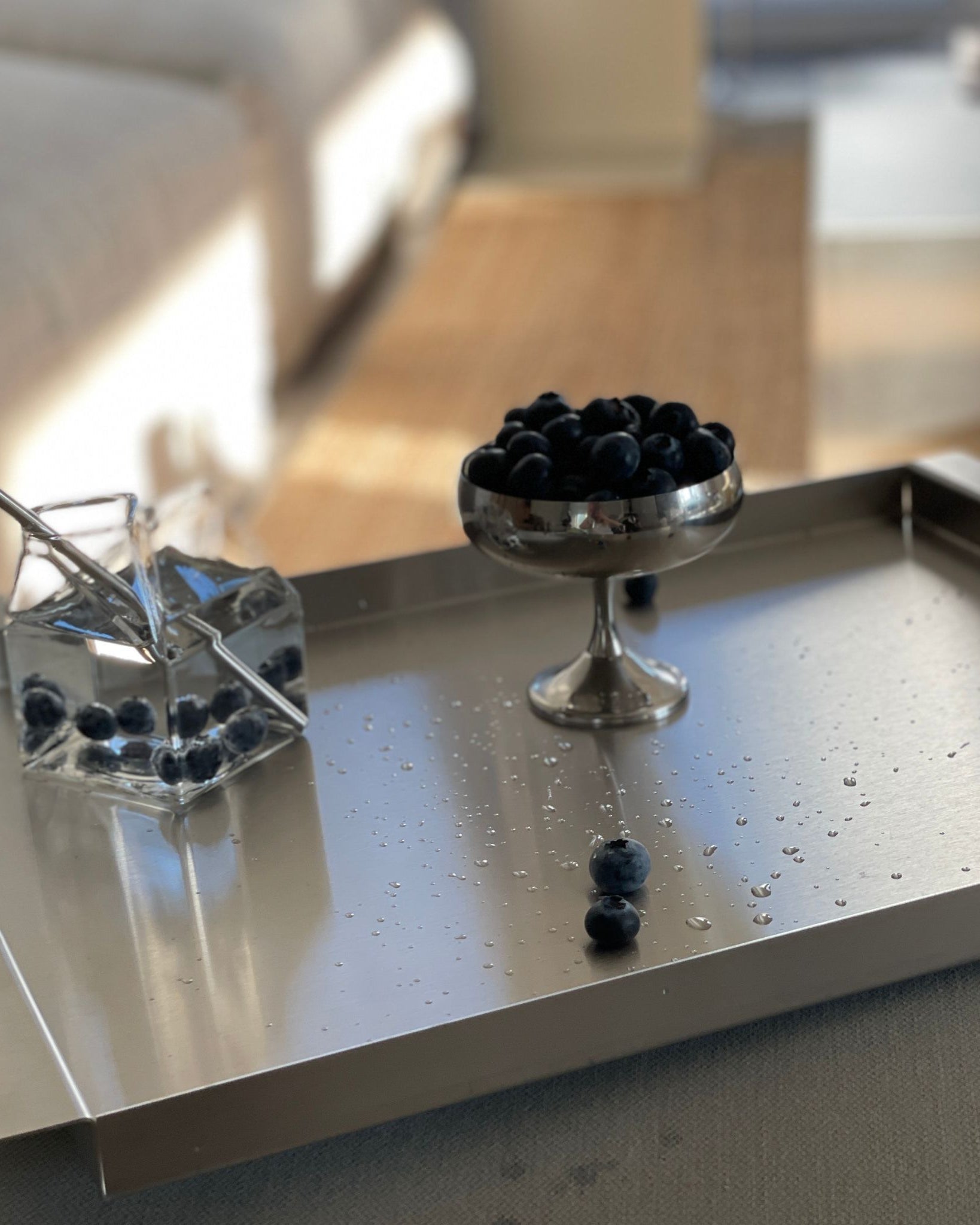 edelstahl tablett mit blaubeeren wasserkaraffe und tageslicht im wohnzimmer