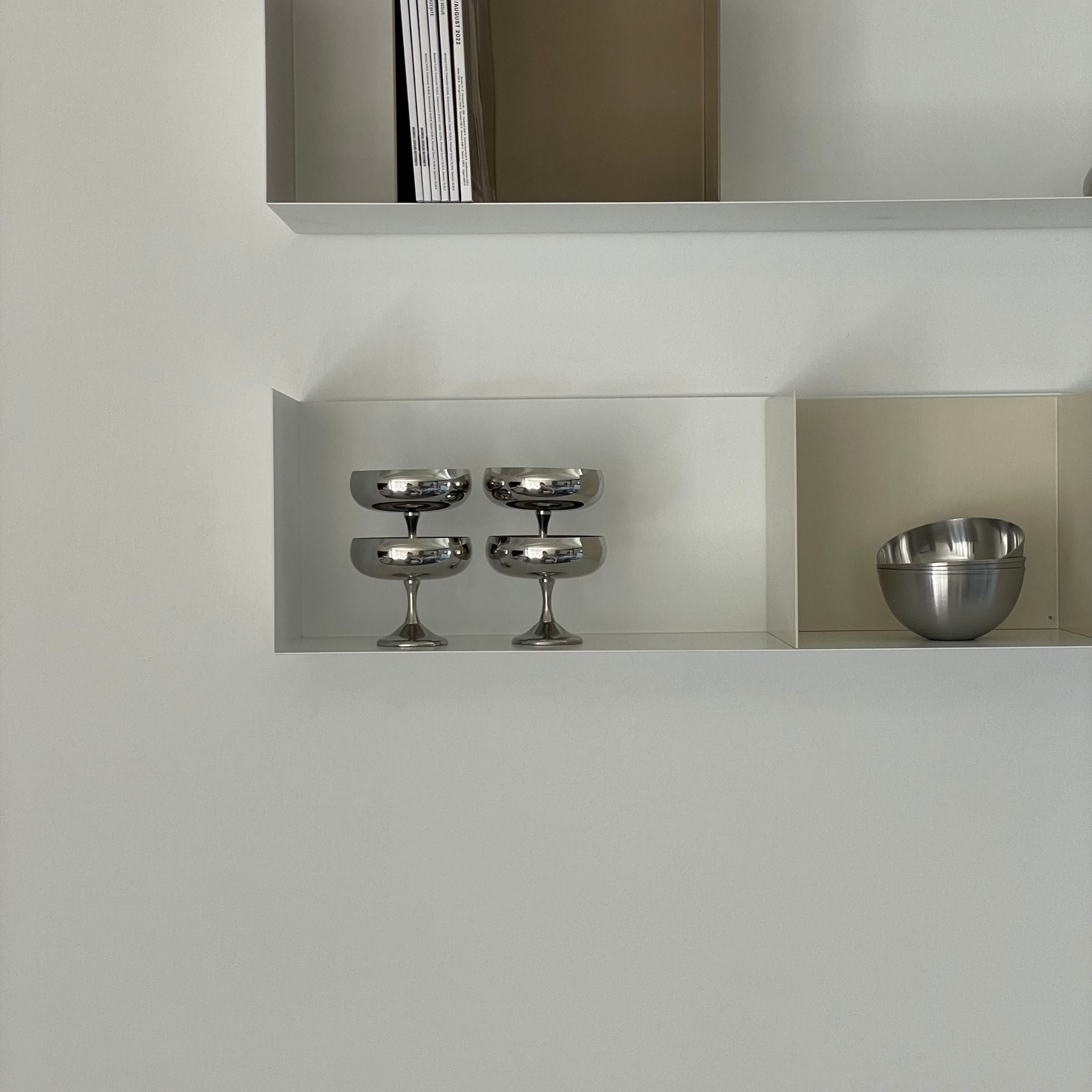 Weißes Wandregal mit Buchstützen in Cremeweiß und Graubeige, dekoriert mit Edelstahl-Schalen und Gläsern