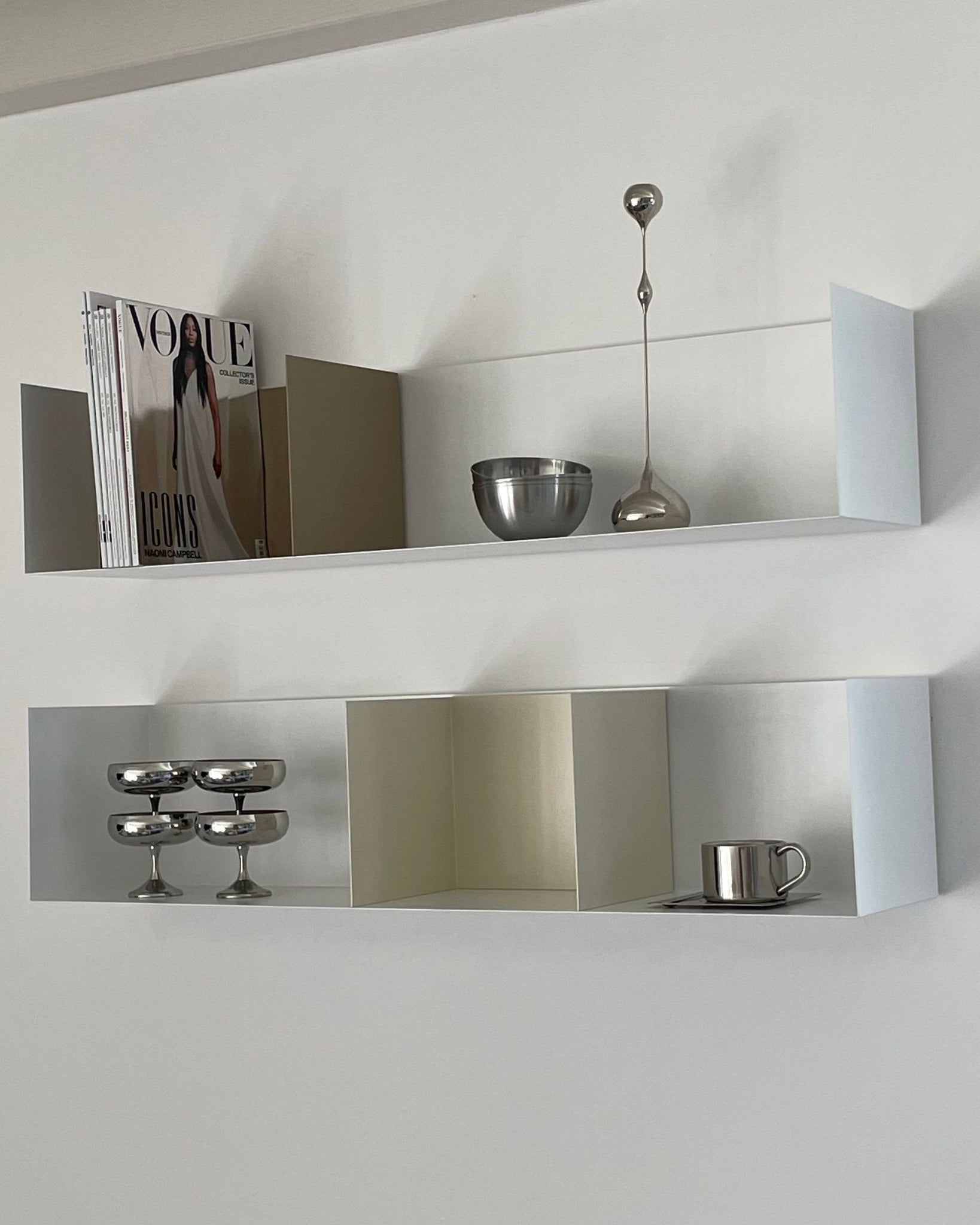 Weißes Wandregal mit Buchstützen in Cremeweiß und Graubeige, dekoriert mit Edelstahl-Accessoires und Magazinen