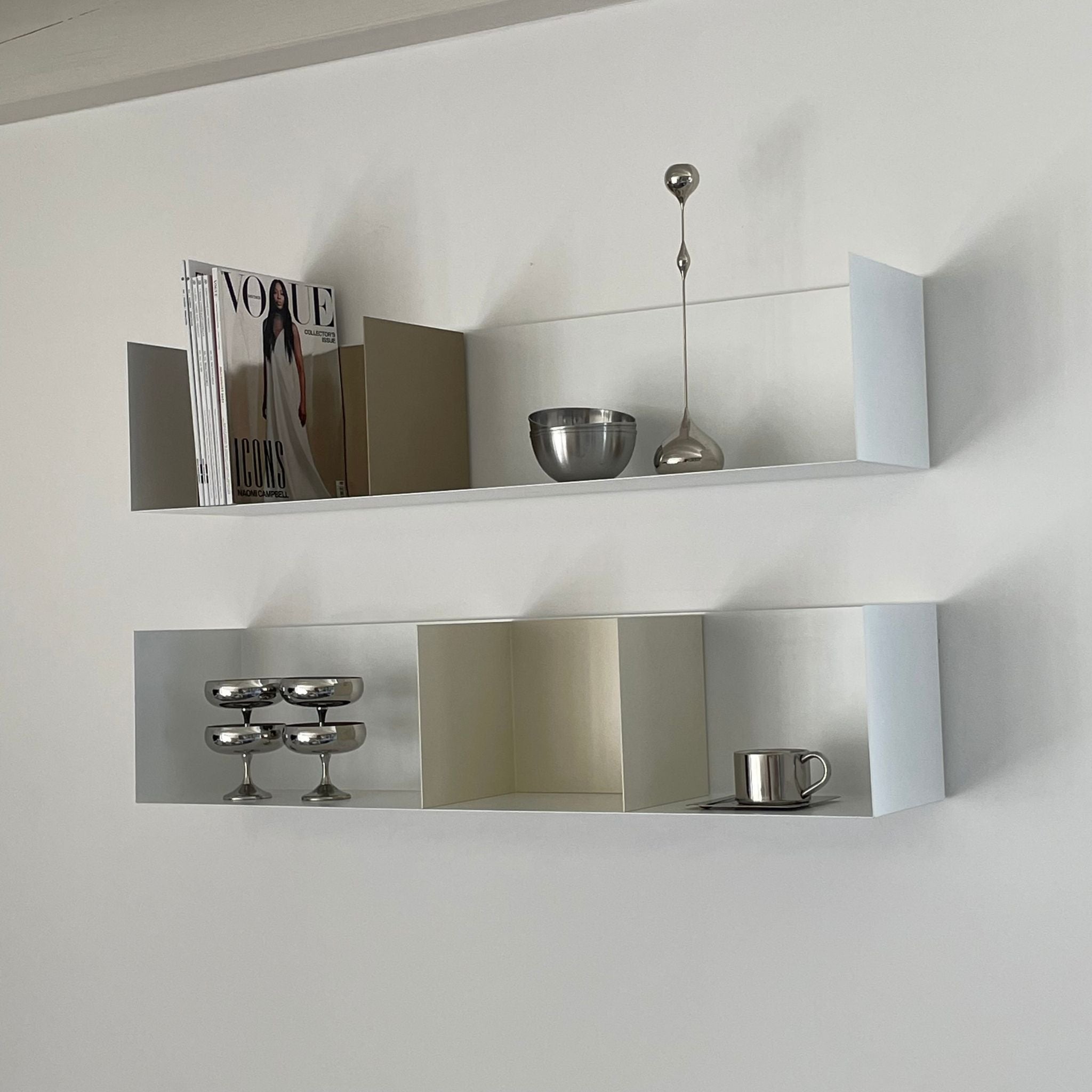 Weißes Wandregal mit Buchstützen in Cremeweiß und Graubeige, dekoriert mit Edelstahl-Accessoires und Magazinen