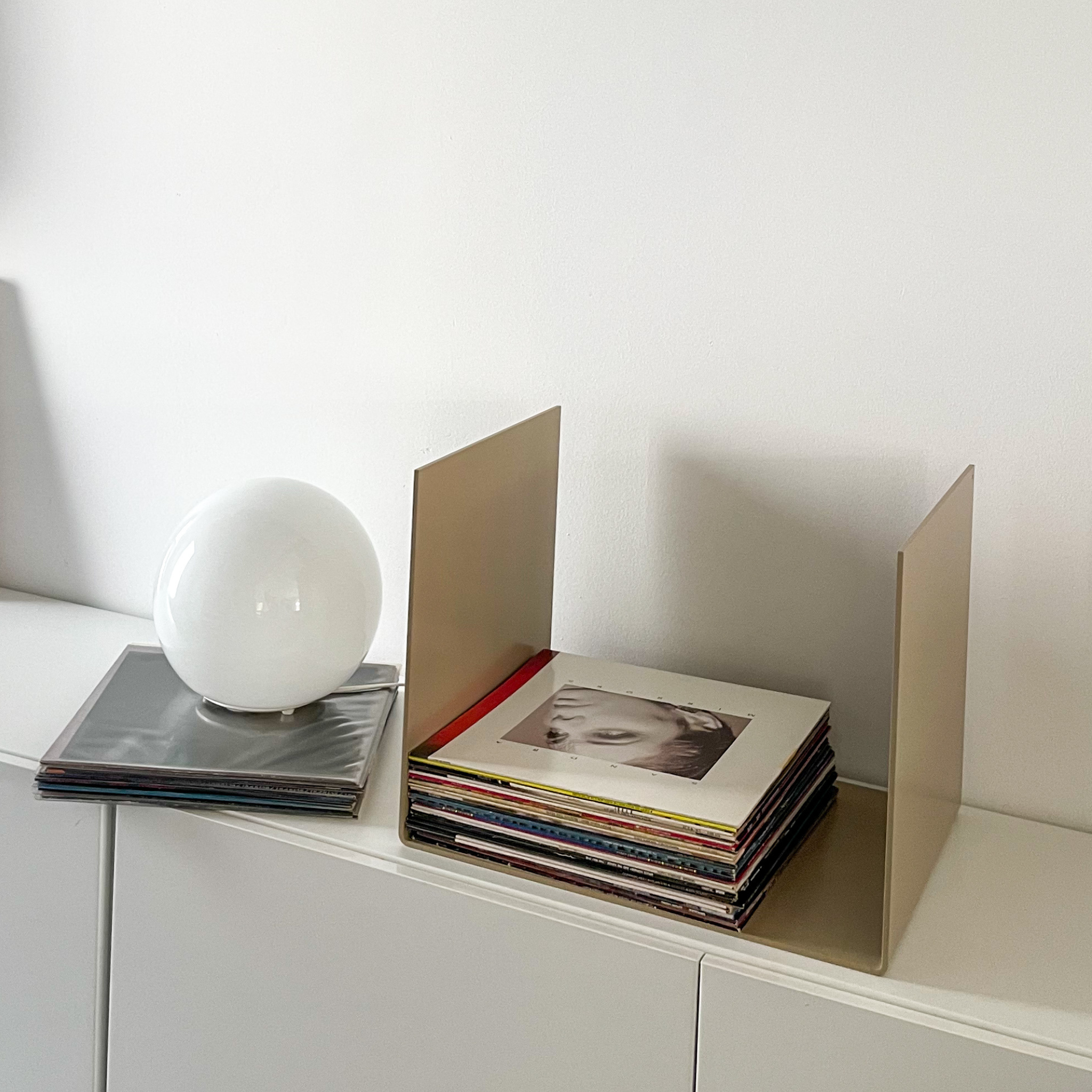 Nahaufnahme einer graubeigen Metallablage auf einer weißen Kommode, dekoriert mit Vinyl-Schallplatten und einem gerahmten Kunstobjekt, modernes Wohnaccessoire