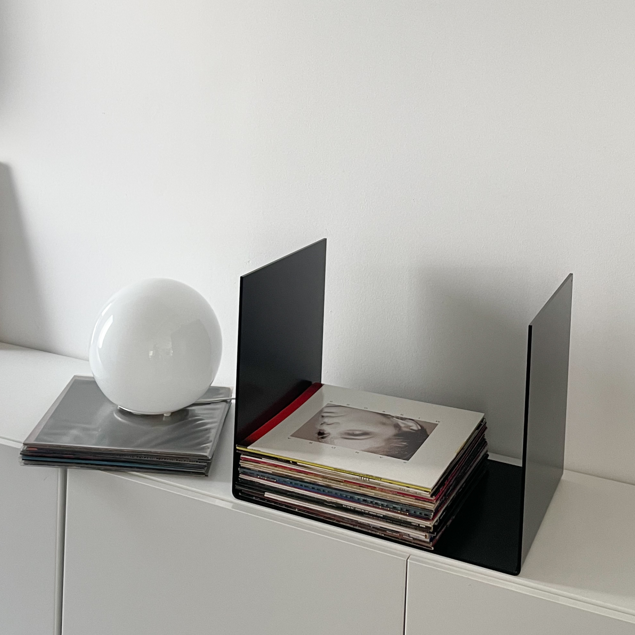 Nahaufnahme einer schwarzen Metallablage auf einer weißen Kommode, dekoriert mit Vinyl-Schallplatten und einem gerahmten Kunstobjekt, modernes Wohnaccessoire