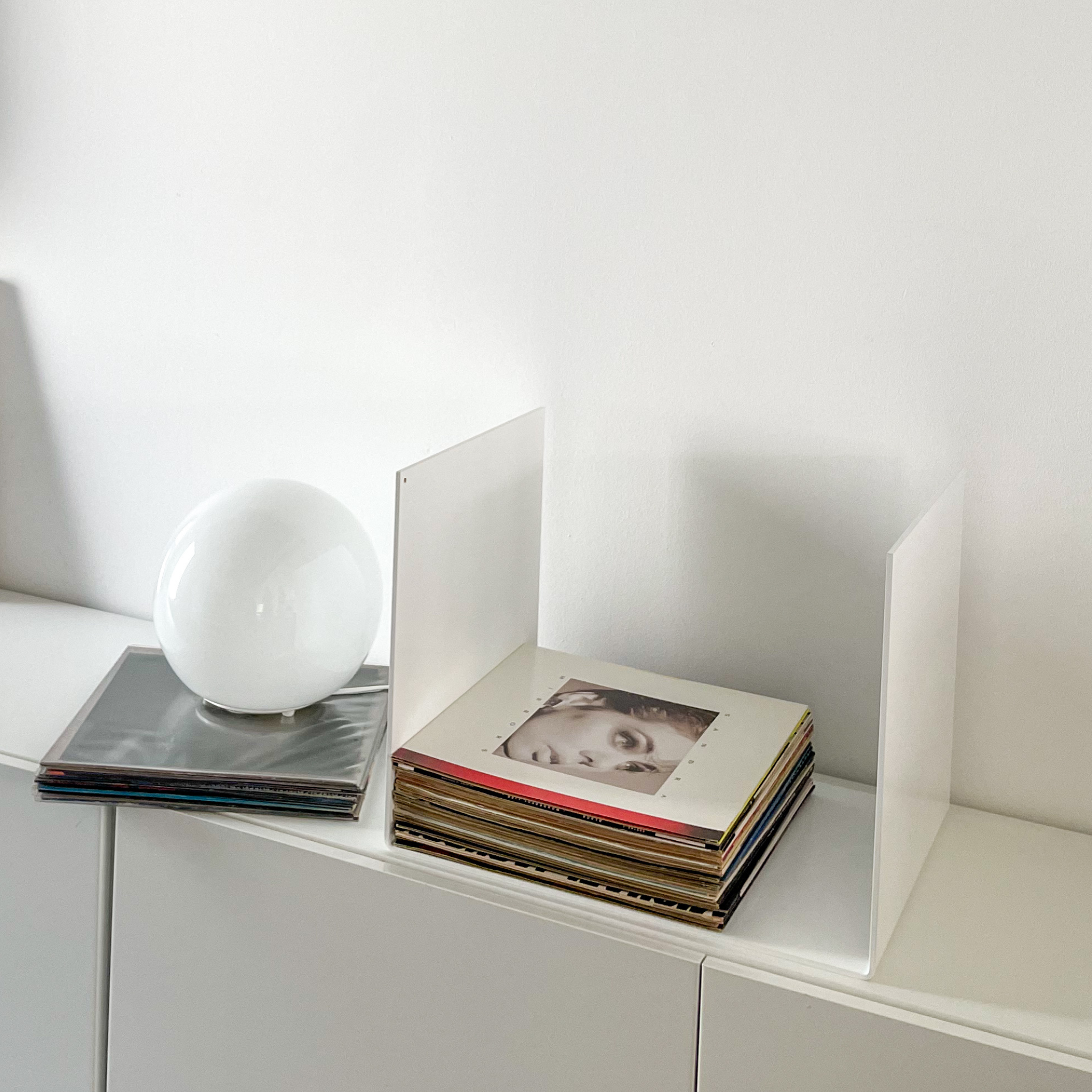 Nahaufnahme einer weißen Metallablage auf einer weißen Kommode, dekoriert mit Vinyl-Schallplatten und einem gerahmten Kunstobjekt, modernes Wohnaccessoire