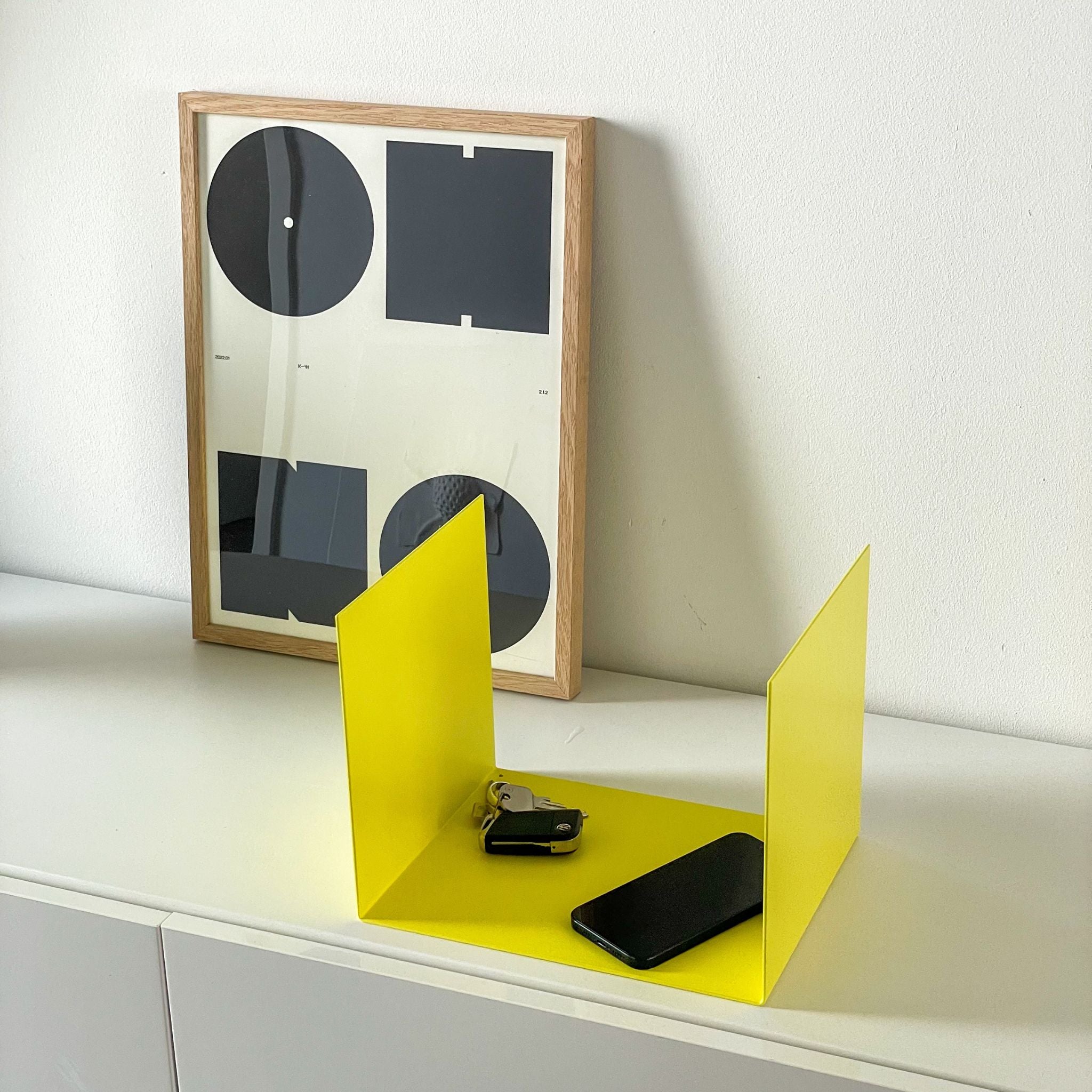 Kleine gelbe Ablage auf einer Kommode im Flur, dekoriert mit einem Bildrahmen, Smartphone und Schlüsseln
