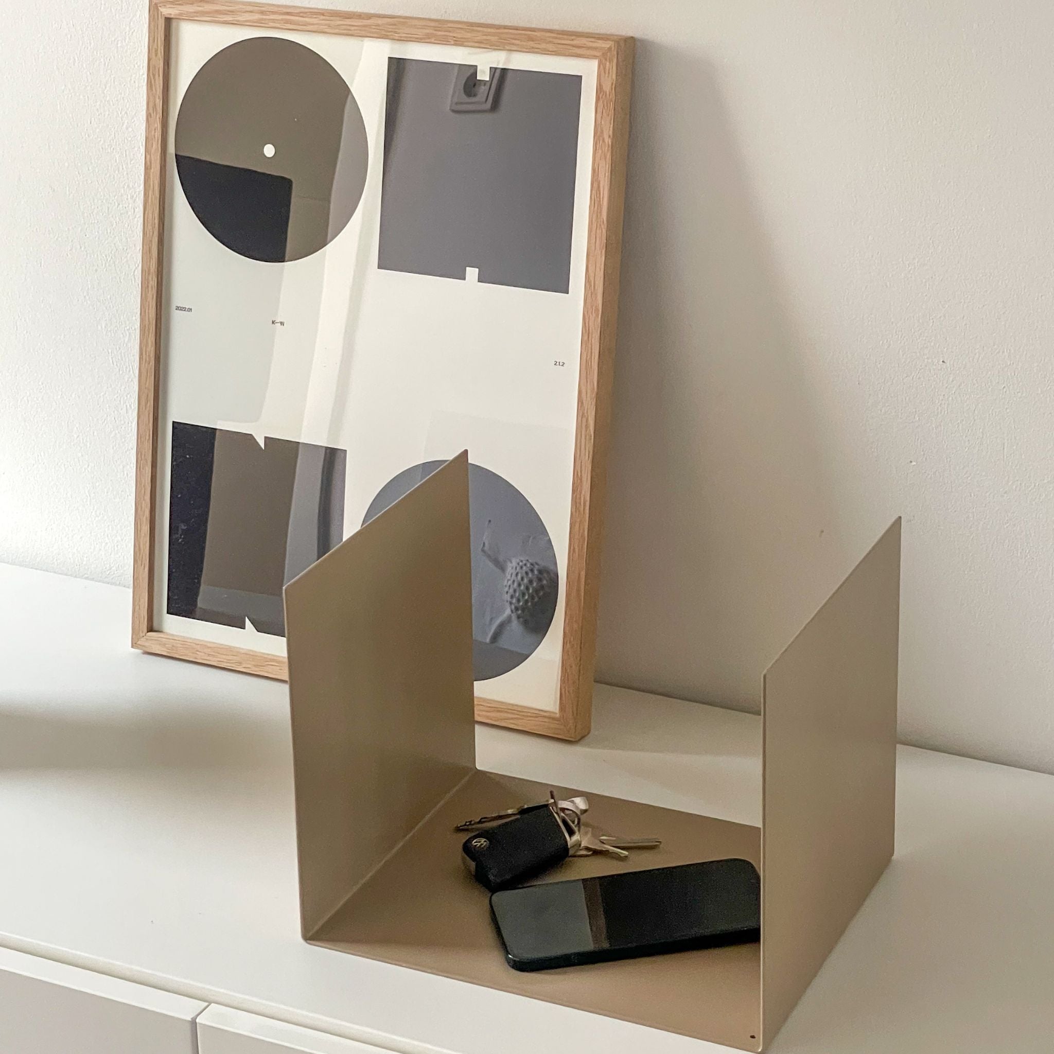 Kleine graubeige Ablage auf einer Kommode im Flur, dekoriert mit einem Bildrahmen, Smartphone und Schlüsseln