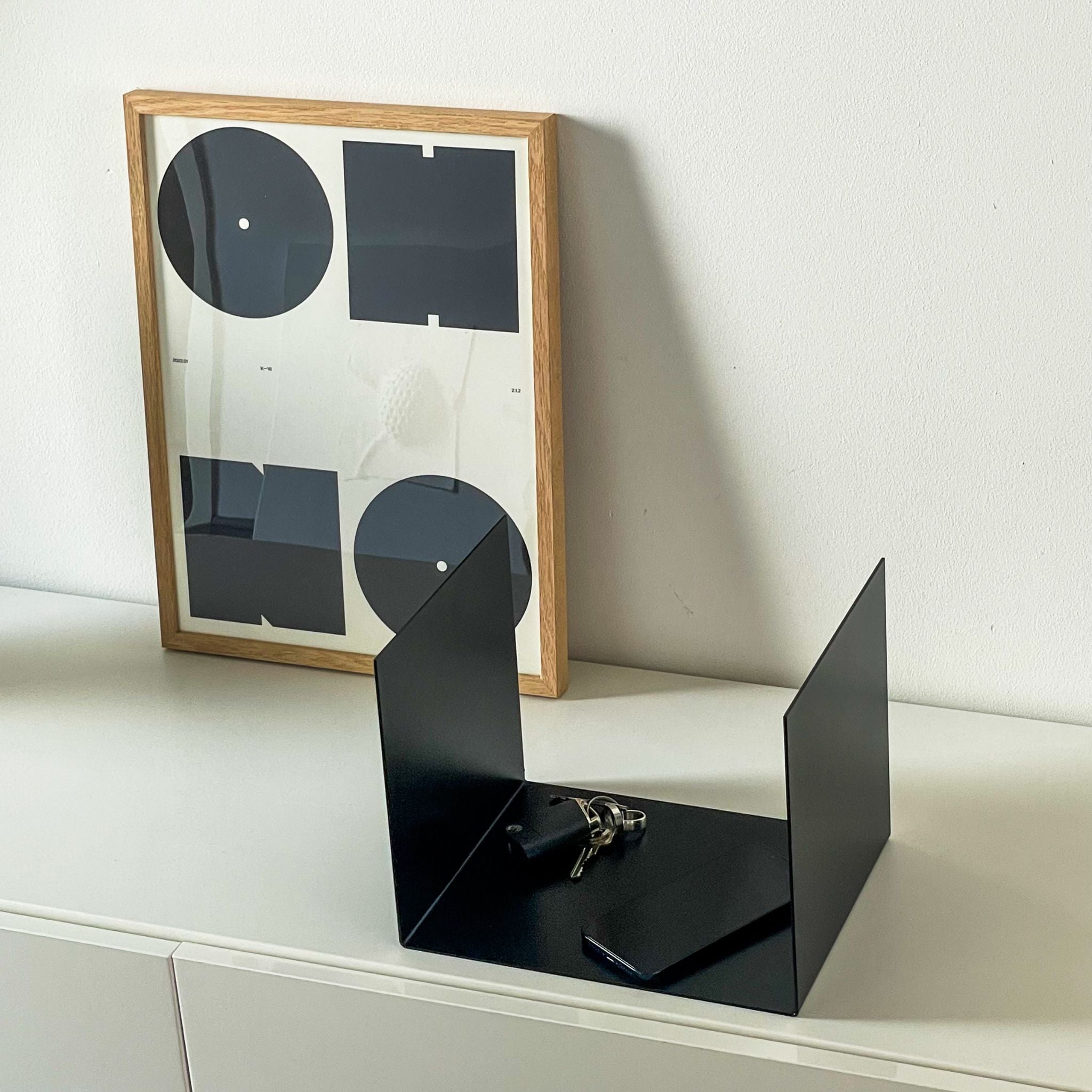 Kleine schwarze Ablage auf einer Kommode im Flur, dekoriert mit einem Bildrahmen, Smartphone und Schlüsseln