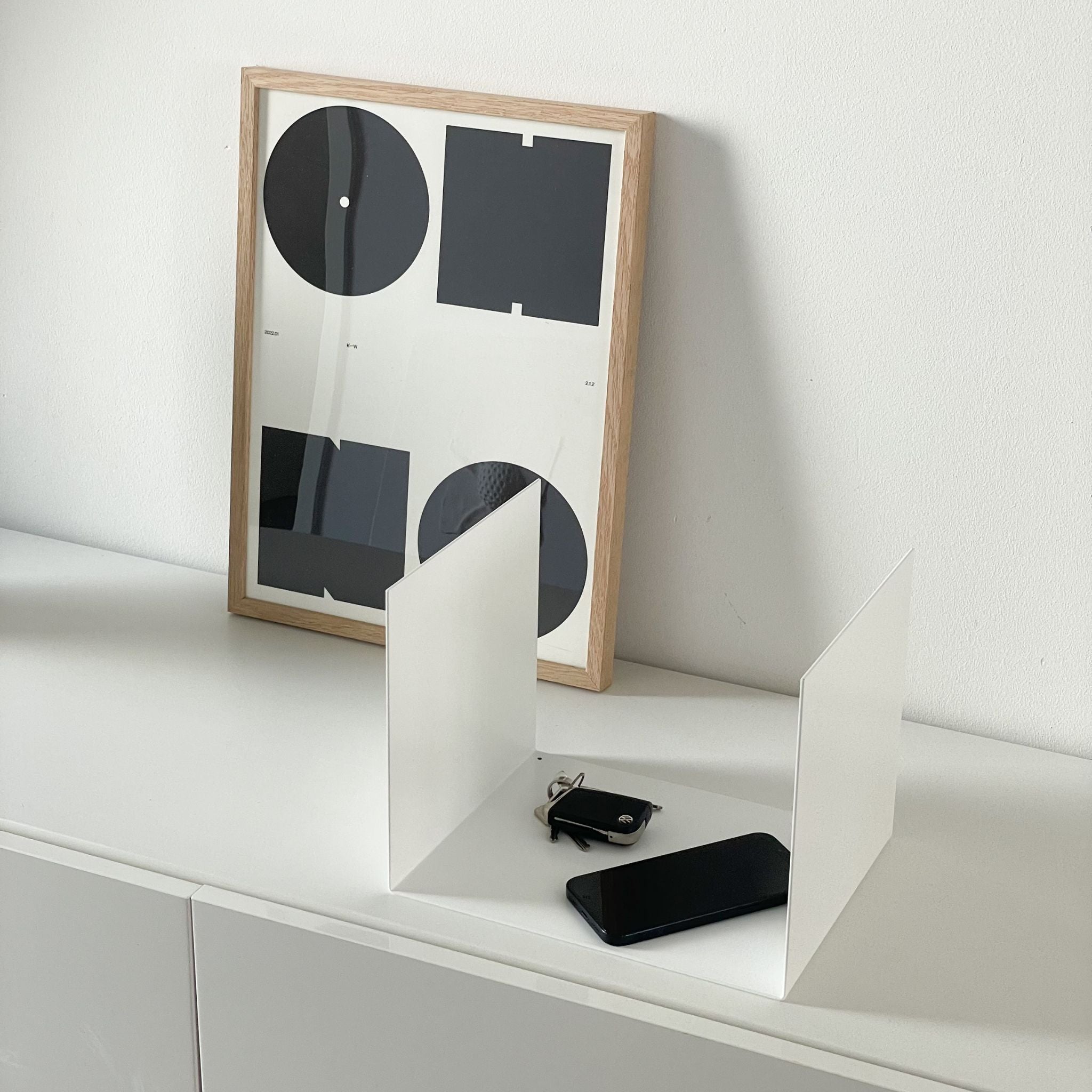 Kleine weiße Ablage auf einer Kommode im Flur, dekoriert mit einem Bildrahmen, Smartphone und Schlüsseln