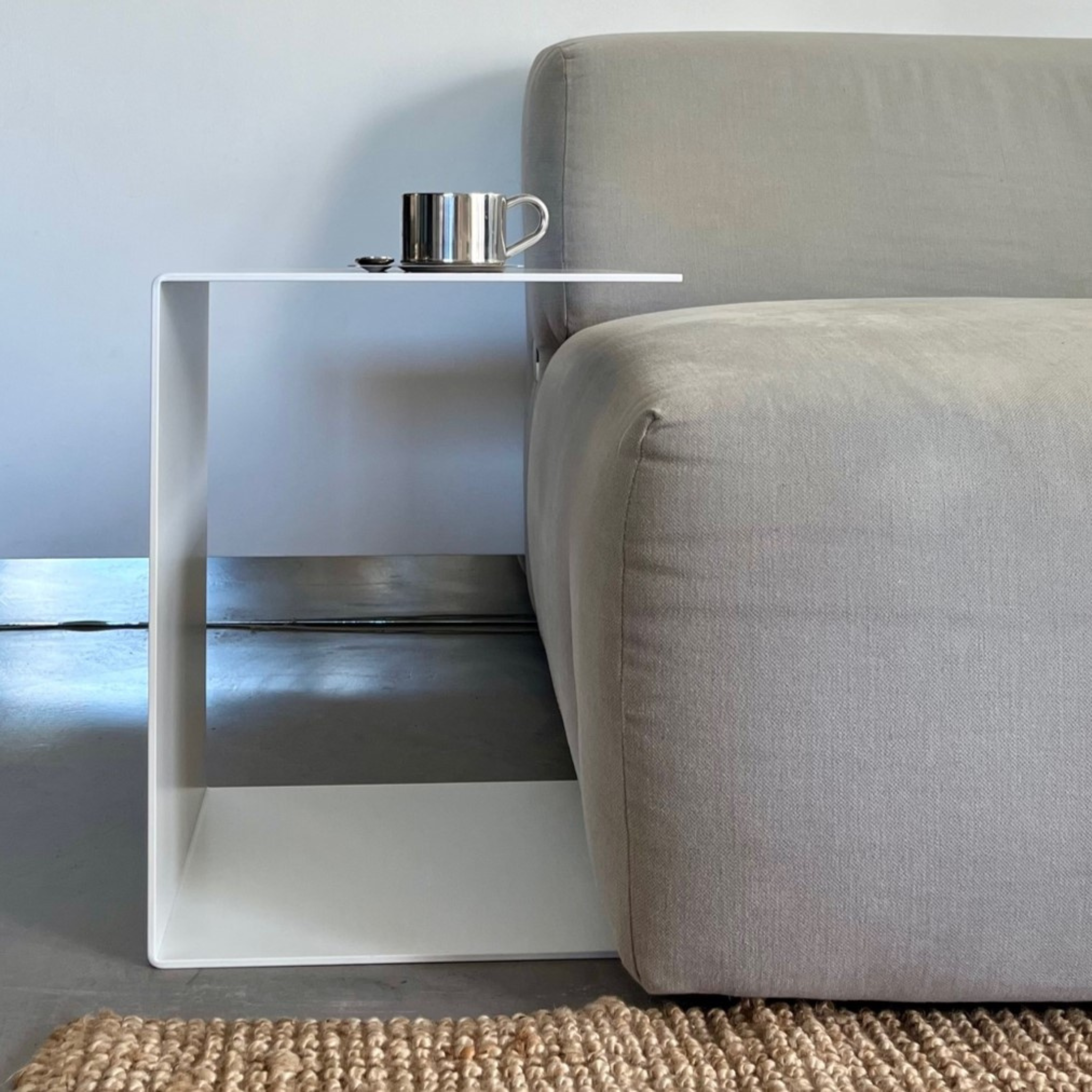 Weißer minimalistischer Beistelltisch aus Metall neben grauem Sofa, modernes Wohnzimmer mit Teppich