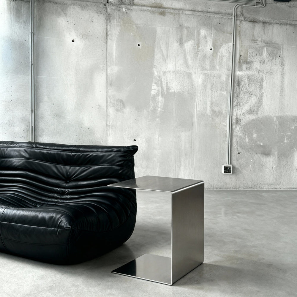 Brushed C neben einem schwarzen Ledersofa, mit sichtbarer Tischhöhe und Ablagefläche