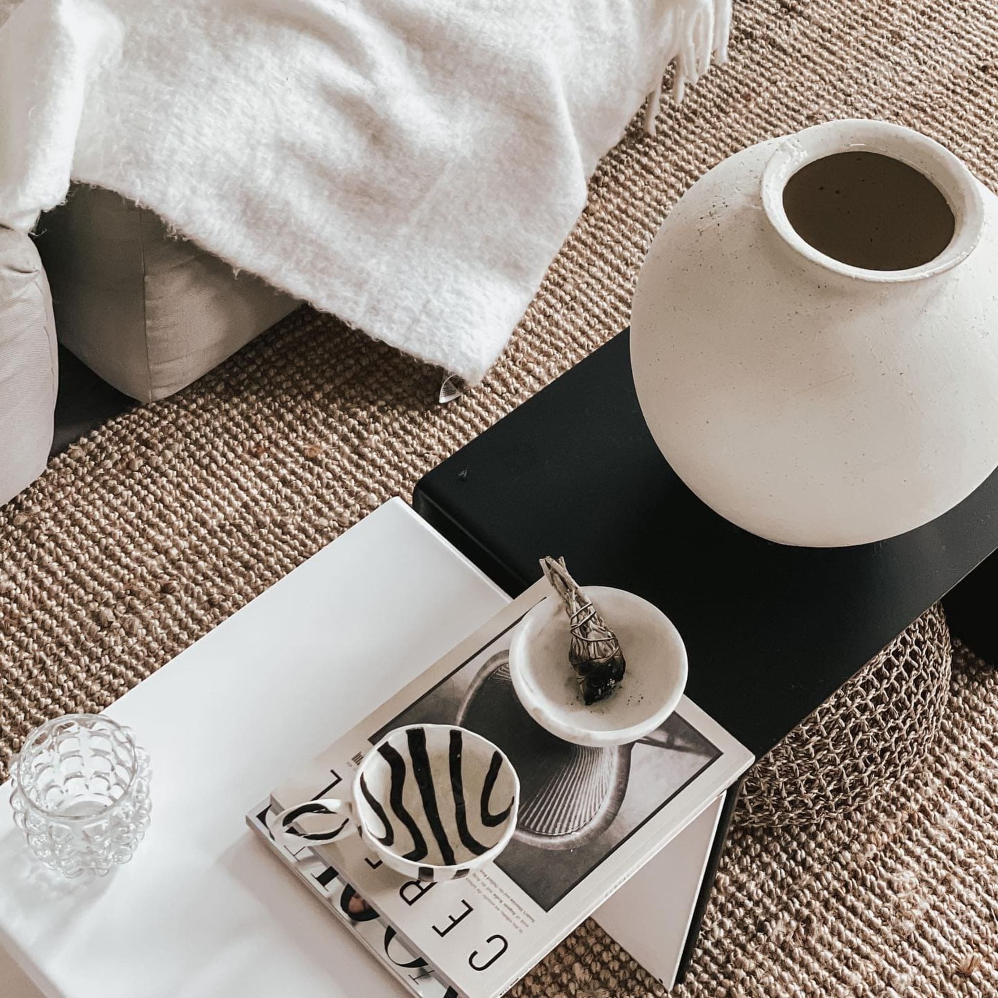 Weiße und schwarze Couchtisch-Kombination mit Keramikvase, Magazinen und Schalen auf geflochtenem Teppich