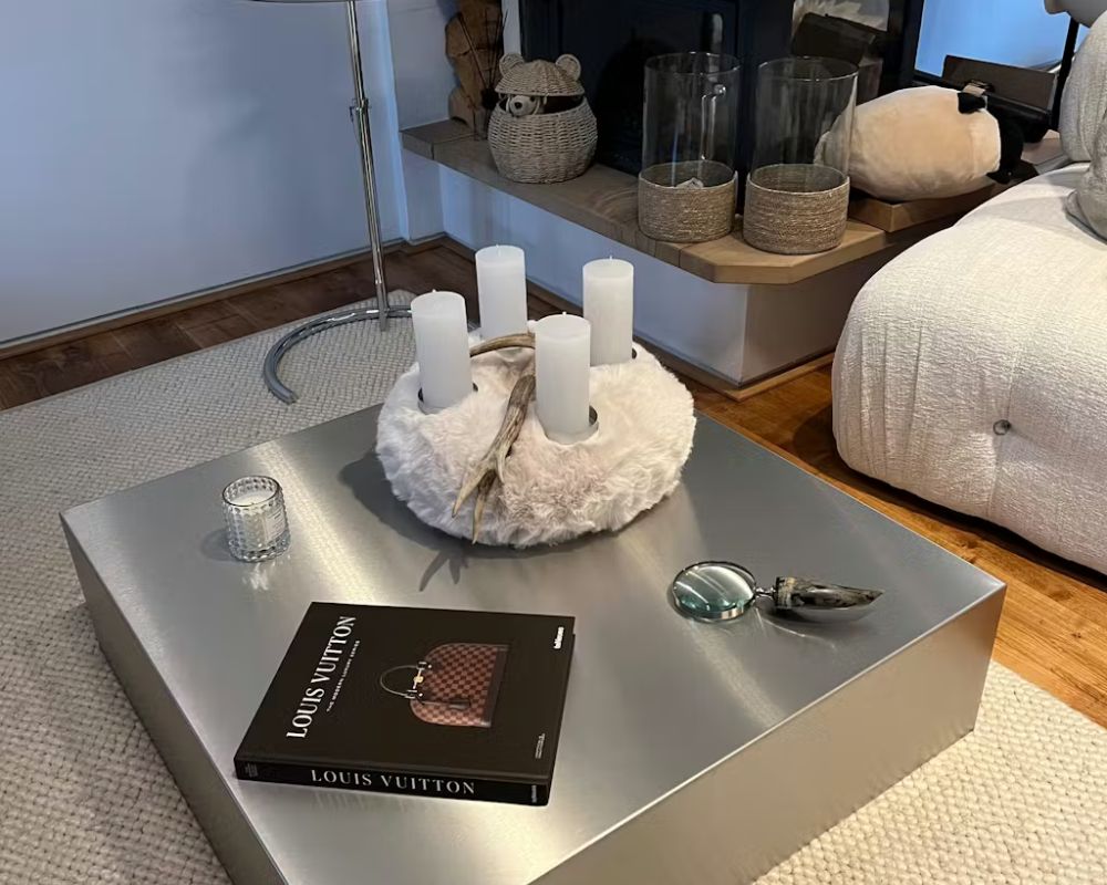 Brushed Q Couchtisch aus gebürstetem Edelstahl im Wohnzimmer mit Kerzendekoration, Coffee-Table-Book und Wohnaccessoires